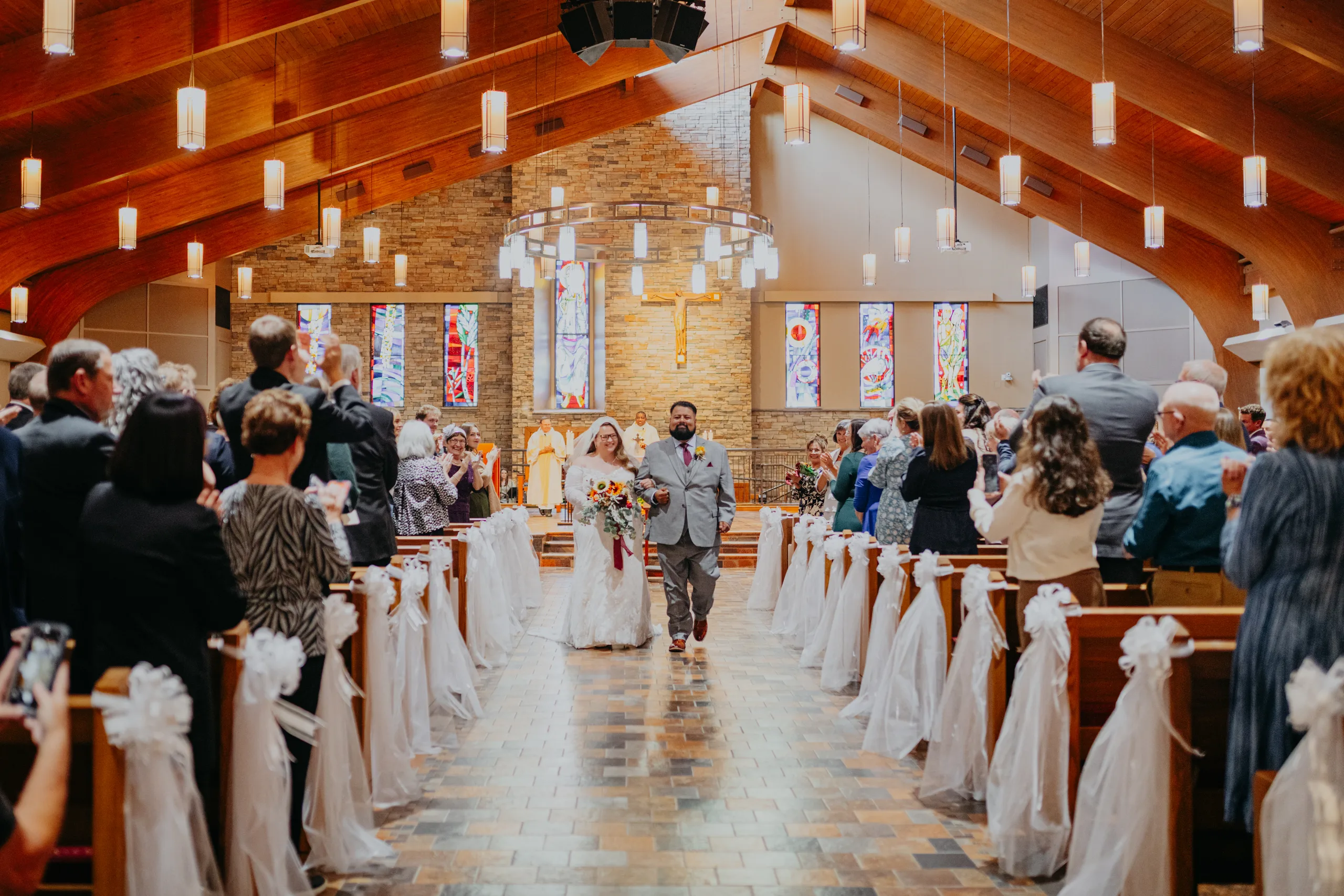 Wedding Ceremony: walking back up the aisle past the tulle-tied pews, at their wedding at St. Lawrence Catholic Church in Lawrenceville, GA