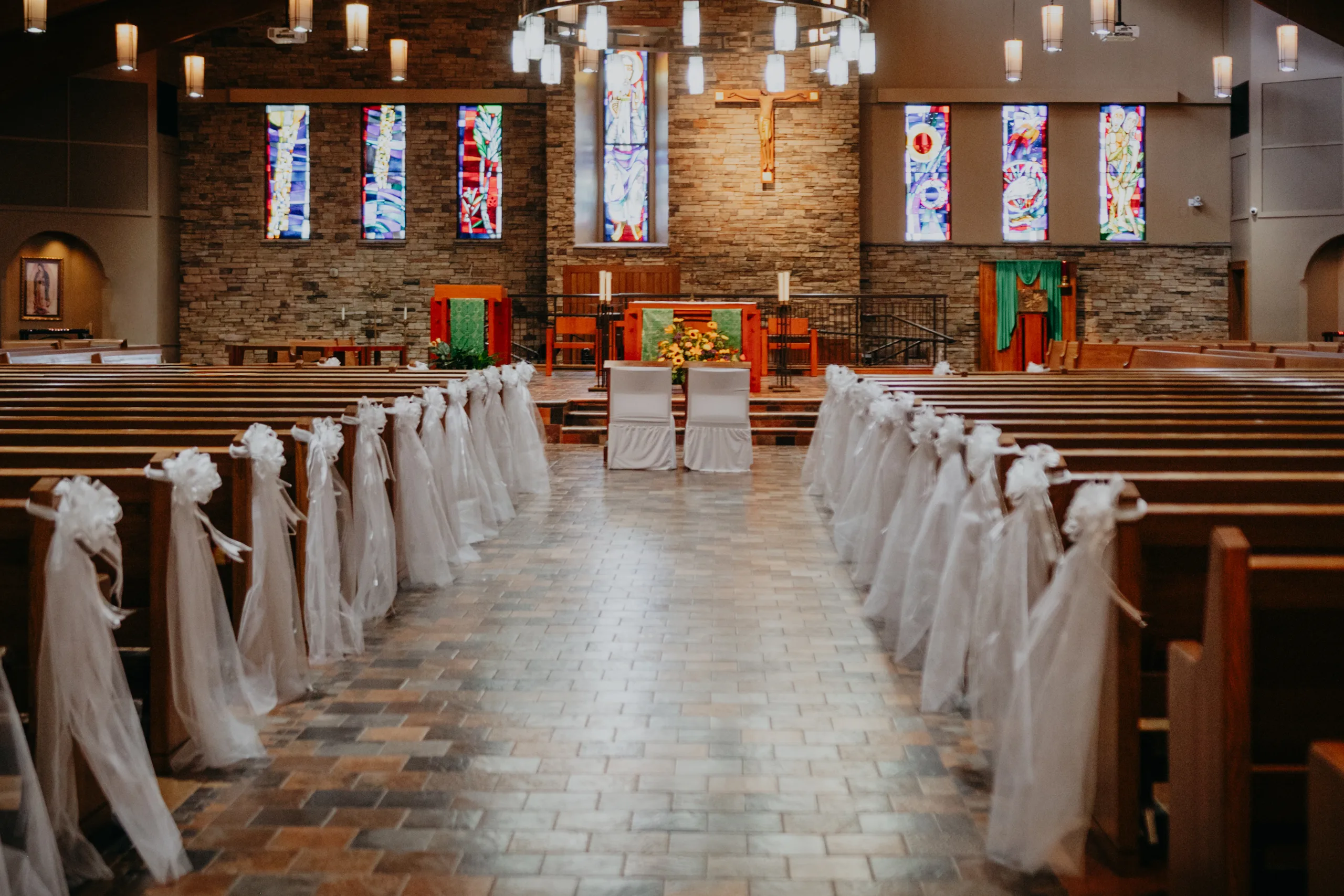 Wedding Ceremony: the aisle and pews tied with tulle, sunflowers on the altar, at a wedding at St. Lawrence Catholic Church in Lawrenceville, GA