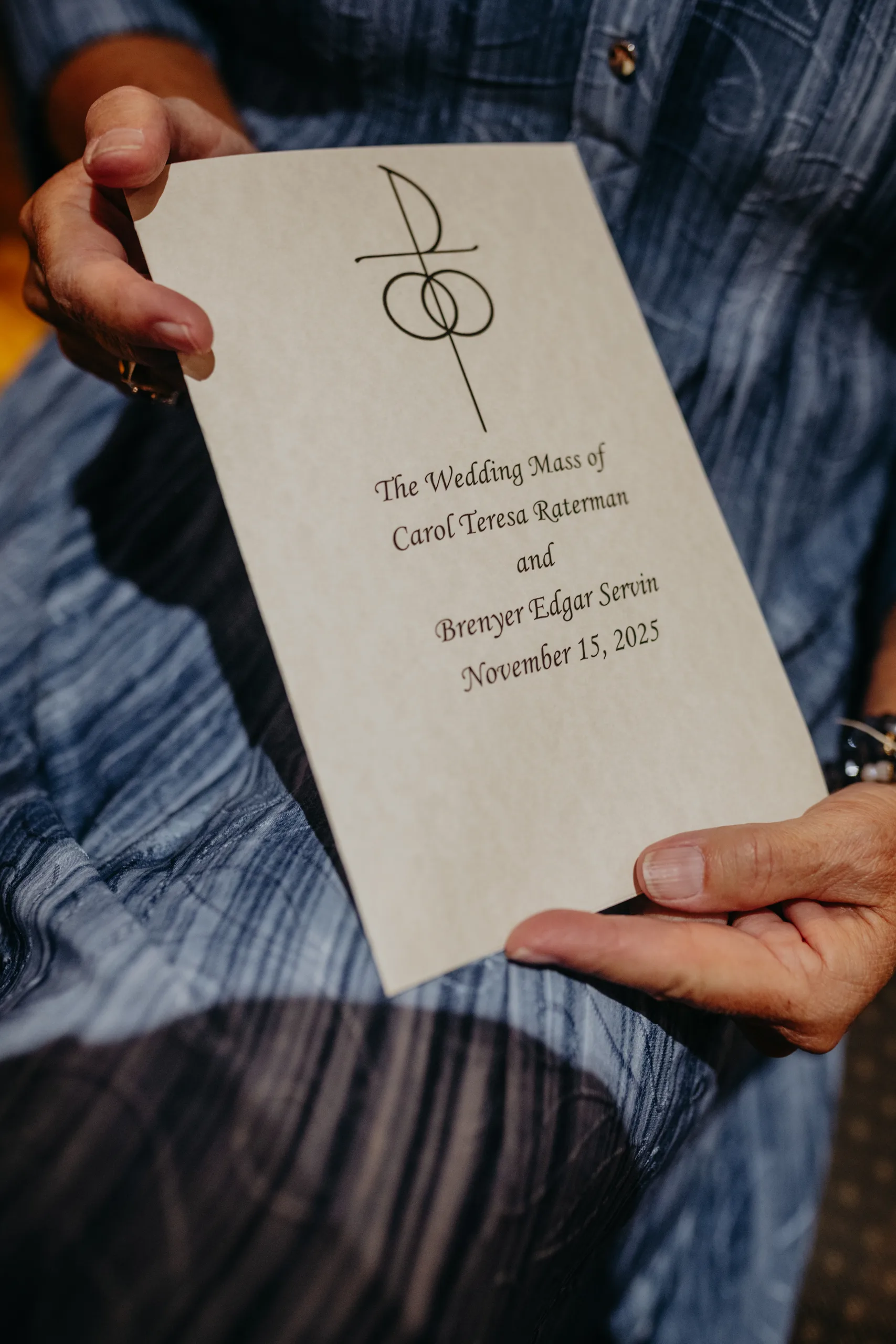 Wedding Ceremony: a guest holding the Wedding Mass program, at their wedding at St. Lawrence Catholic Church in Lawrenceville, GA