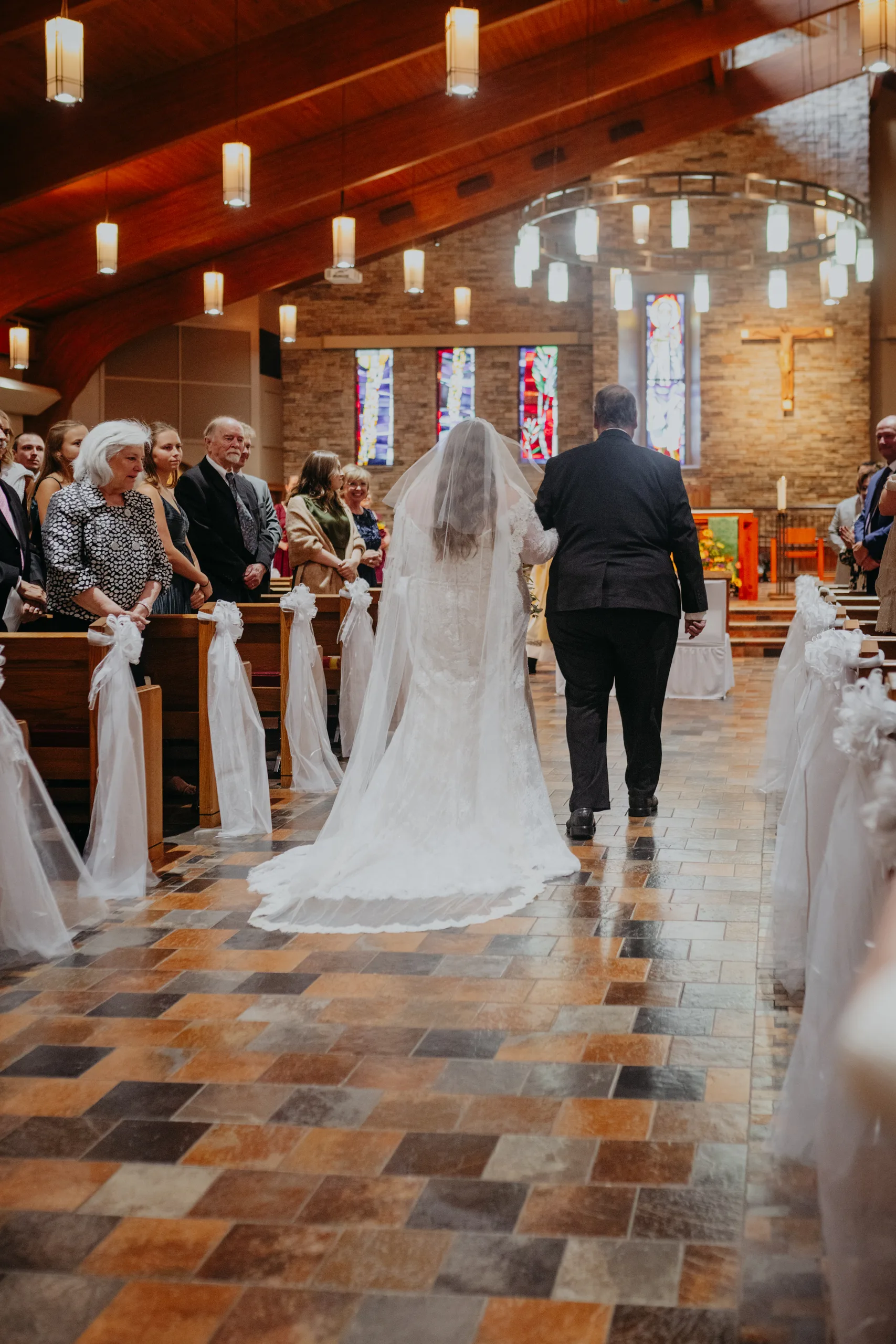 Wedding Ceremony: her dad walking her down the aisle, her cathedral veil behind her, at their wedding at St. Lawrence Catholic Church in Lawrenceville, GA