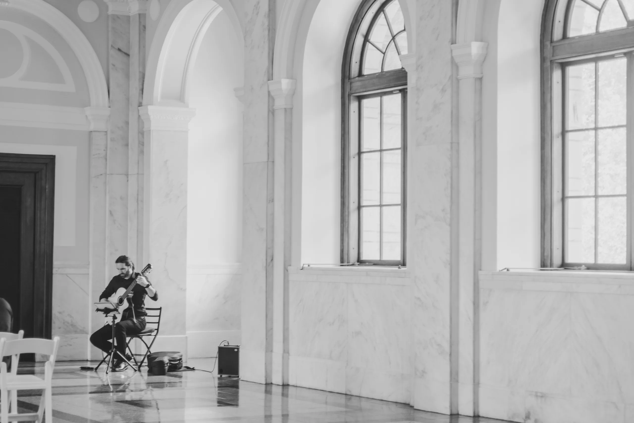 Wedding Ceremony: a guitarist playing in the marble hall, in black and white, at their wedding at the Historic DeKalb Courthouse in Decatur, GA