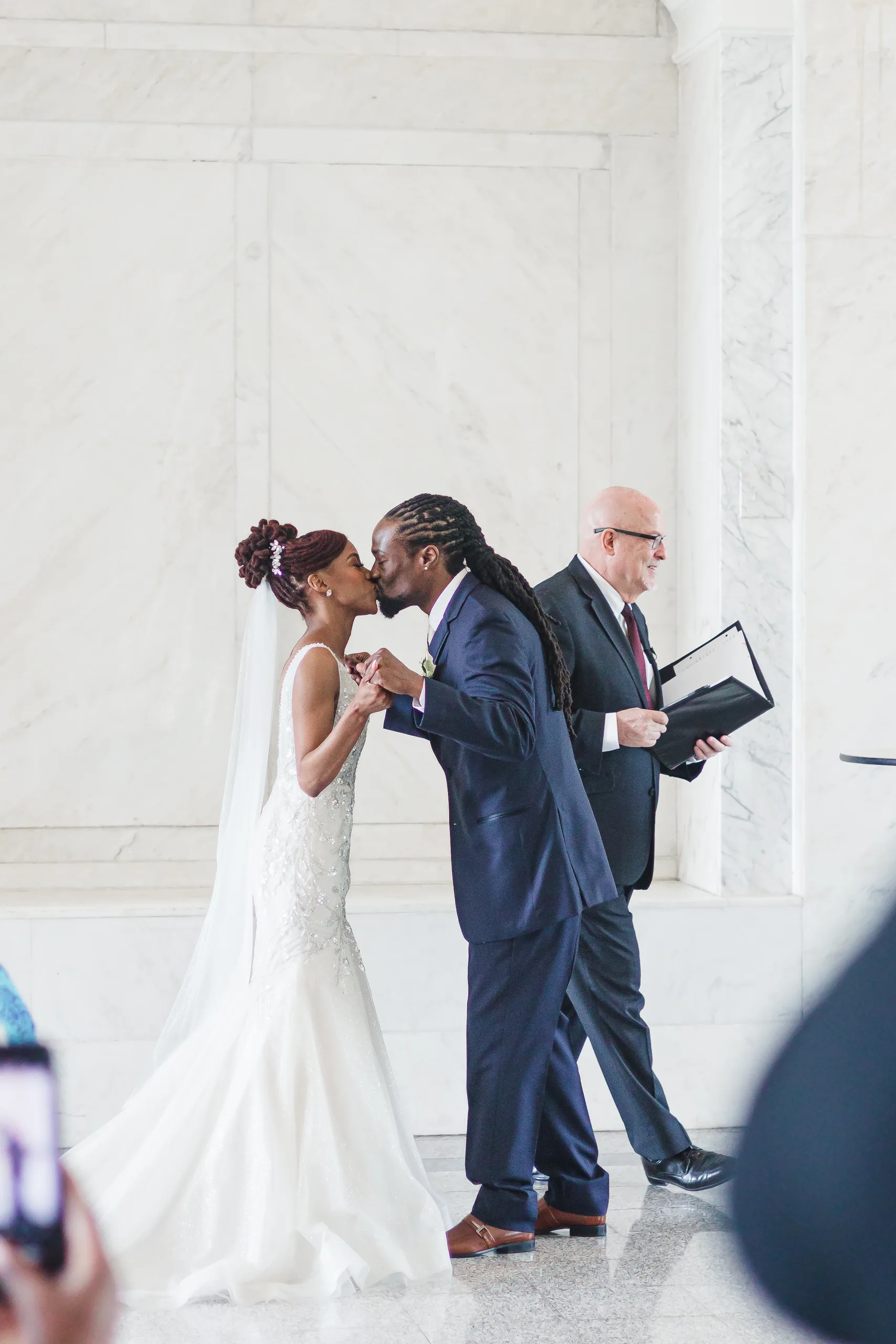 Wedding Ceremony: the first kiss beside the officiant, at their wedding at the Historic DeKalb Courthouse in Decatur, GA