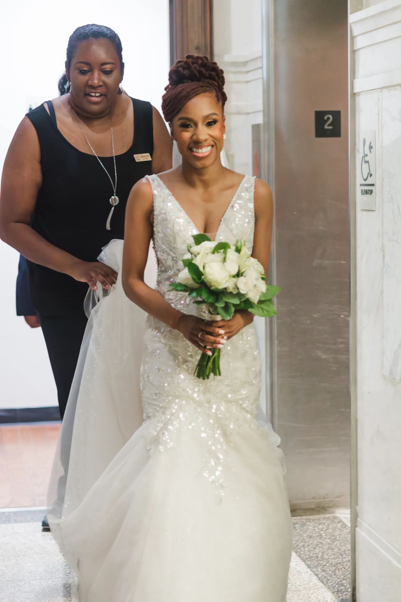Wedding Ceremony: the bride stepping off the elevator with her bouquet of white roses, at their wedding at the Historic DeKalb Courthouse in Decatur, GA