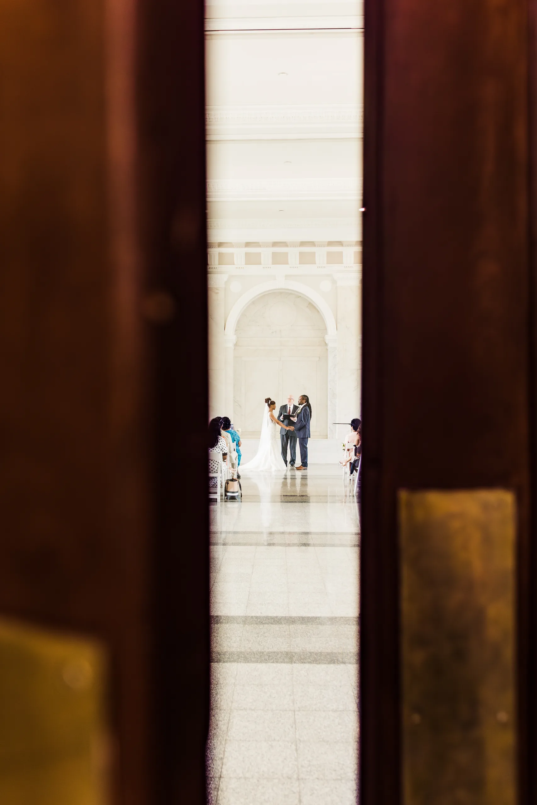 Wedding Ceremony: the ceremony seen through a gap in the wooden doors, at their wedding at the Historic DeKalb Courthouse in Decatur, GA