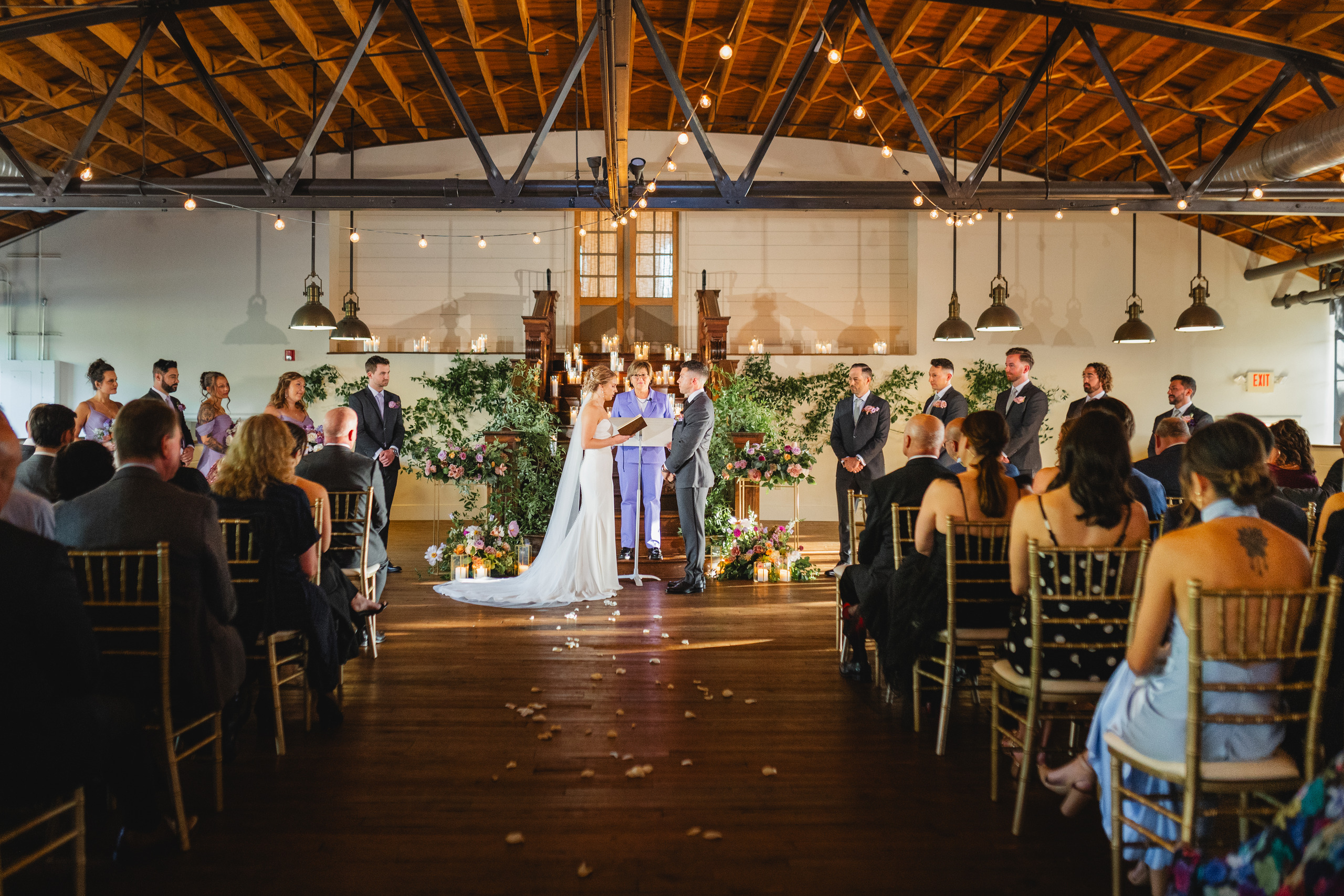 Wedding Ceremony: the aisle from the back of the room, string lights across the barrel-vault ceiling, at a wedding at Summerour Studio in Atlanta, GA
