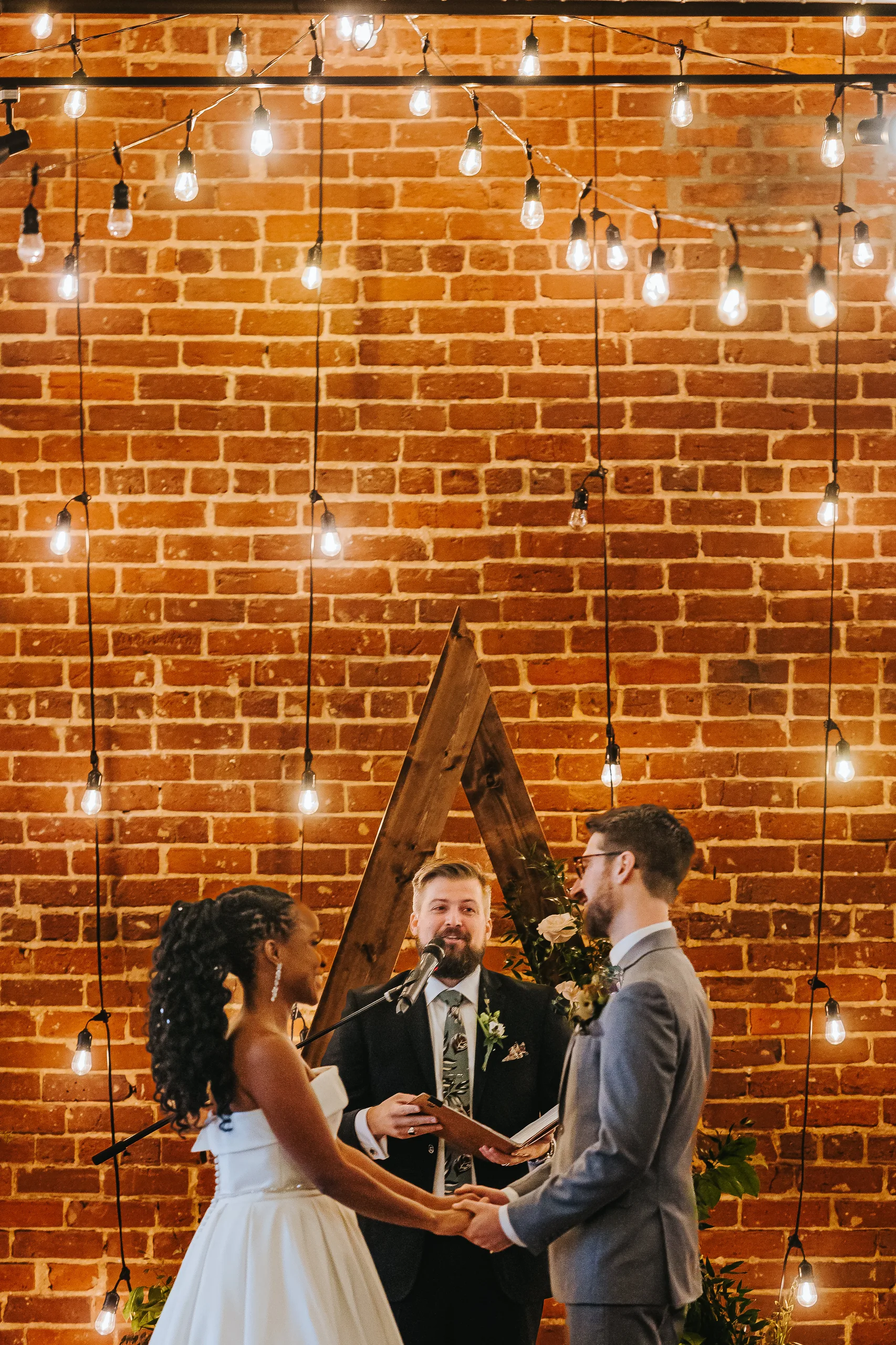 Wedding Ceremony: holding hands in front of the wooden arch and brick wall, at their wedding at Terminus 330 in Atlanta, GA