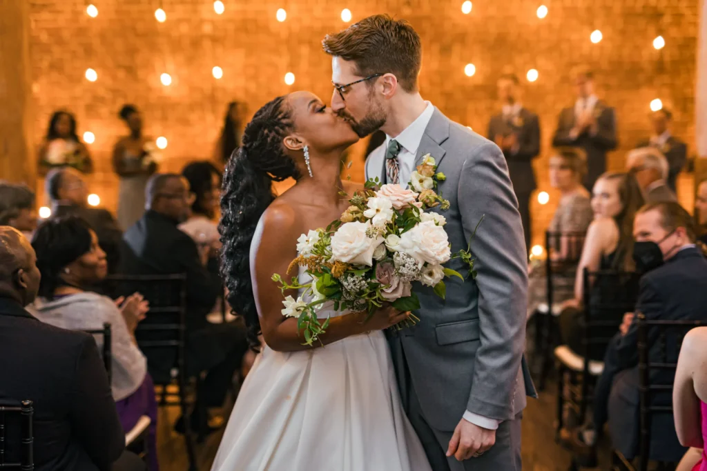 Wedding Ceremony: a kiss with her bouquet as they walk back up the aisle, at their wedding at Terminus 330 in Atlanta, GA