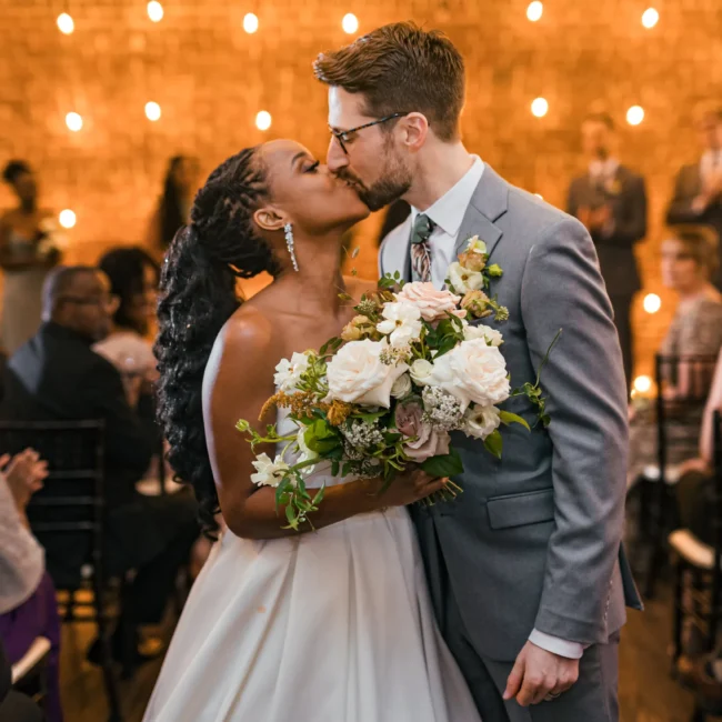 Wedding Ceremony: a kiss with her bouquet as they walk back up the aisle, at their wedding at Terminus 330 in Atlanta, GA