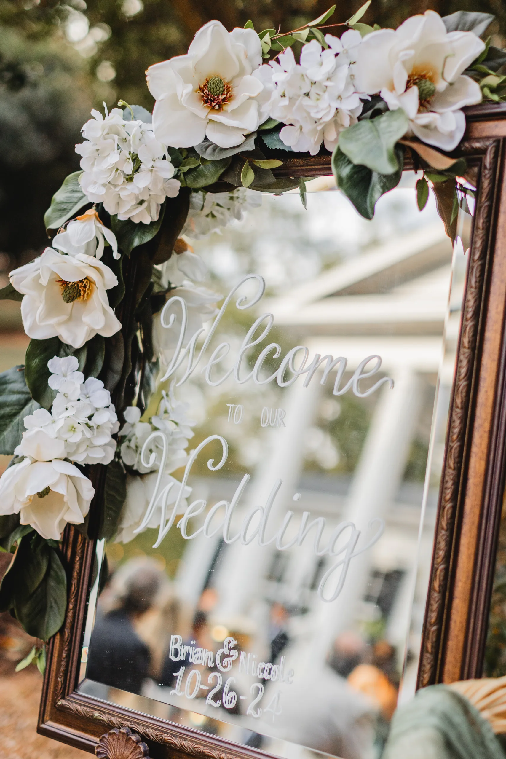 Wedding Details: the welcome mirror with magnolias and hydrangeas, their names and date below, at a wedding at Naylor Hall in Roswell, GA