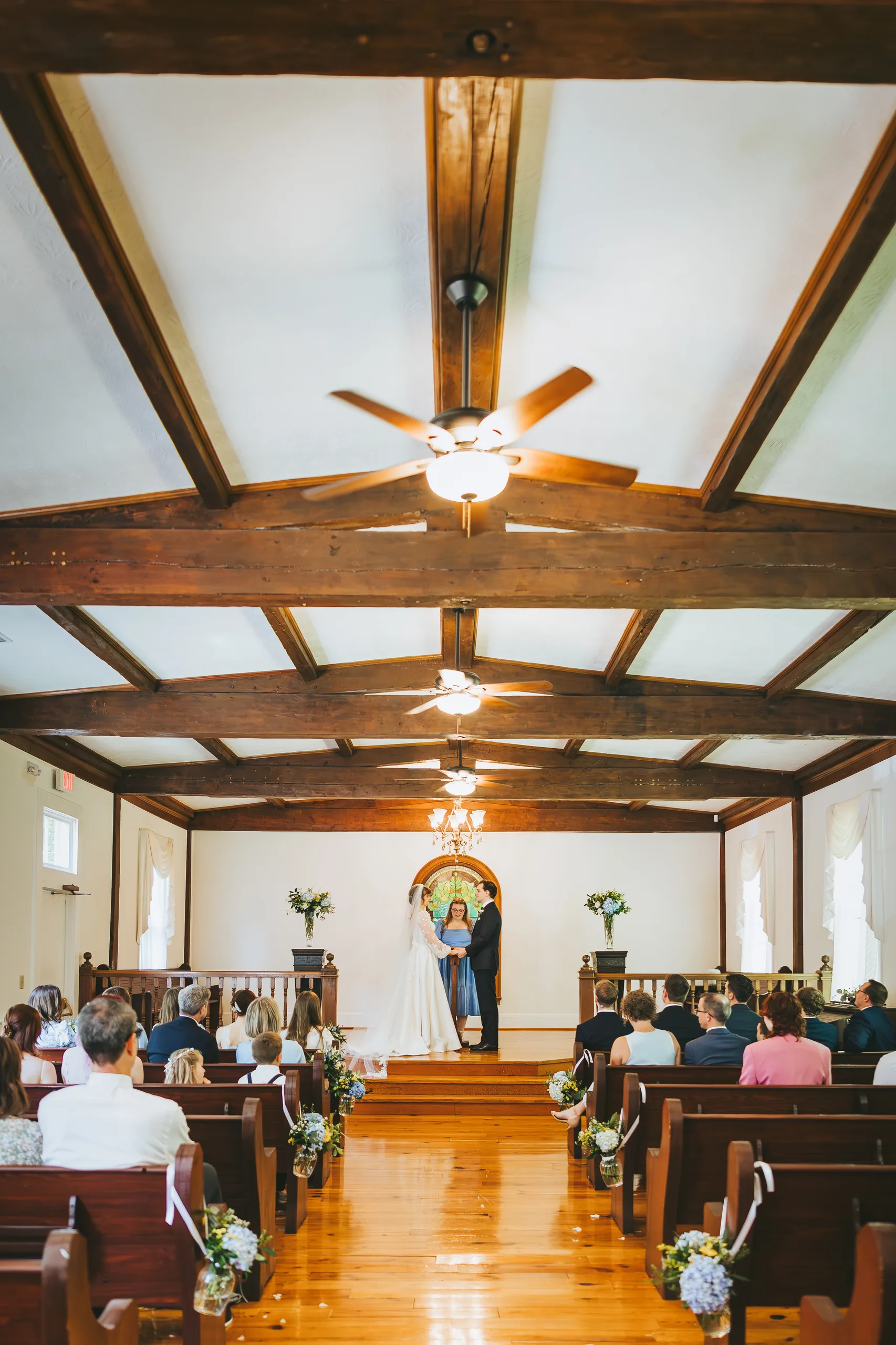 Wedding Ceremony: the chapel from the back, wooden beams overhead, at their wedding at the Chapel at Simpsonwood Park in Peachtree Corners, GA