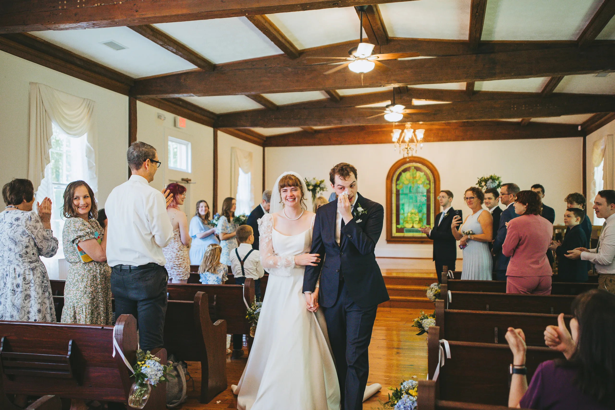 Wedding Ceremony: walking back up the aisle as family cheers, at their wedding at the Chapel at Simpsonwood Park in Peachtree Corners, GA