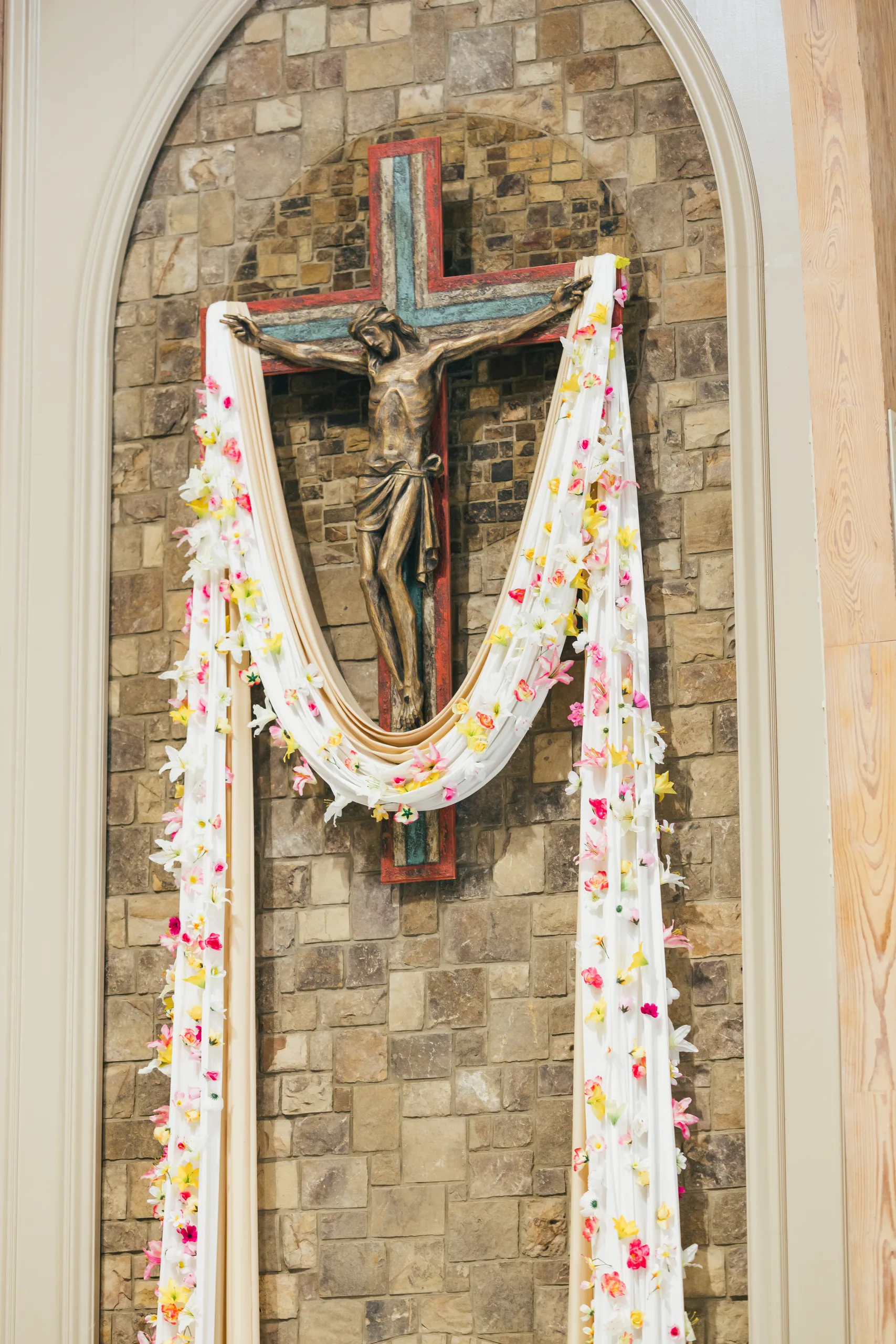 Ceremony Details: the crucifix draped with flowers above the altar at a wedding at Holy Cross Catholic Church in Atlanta, GA