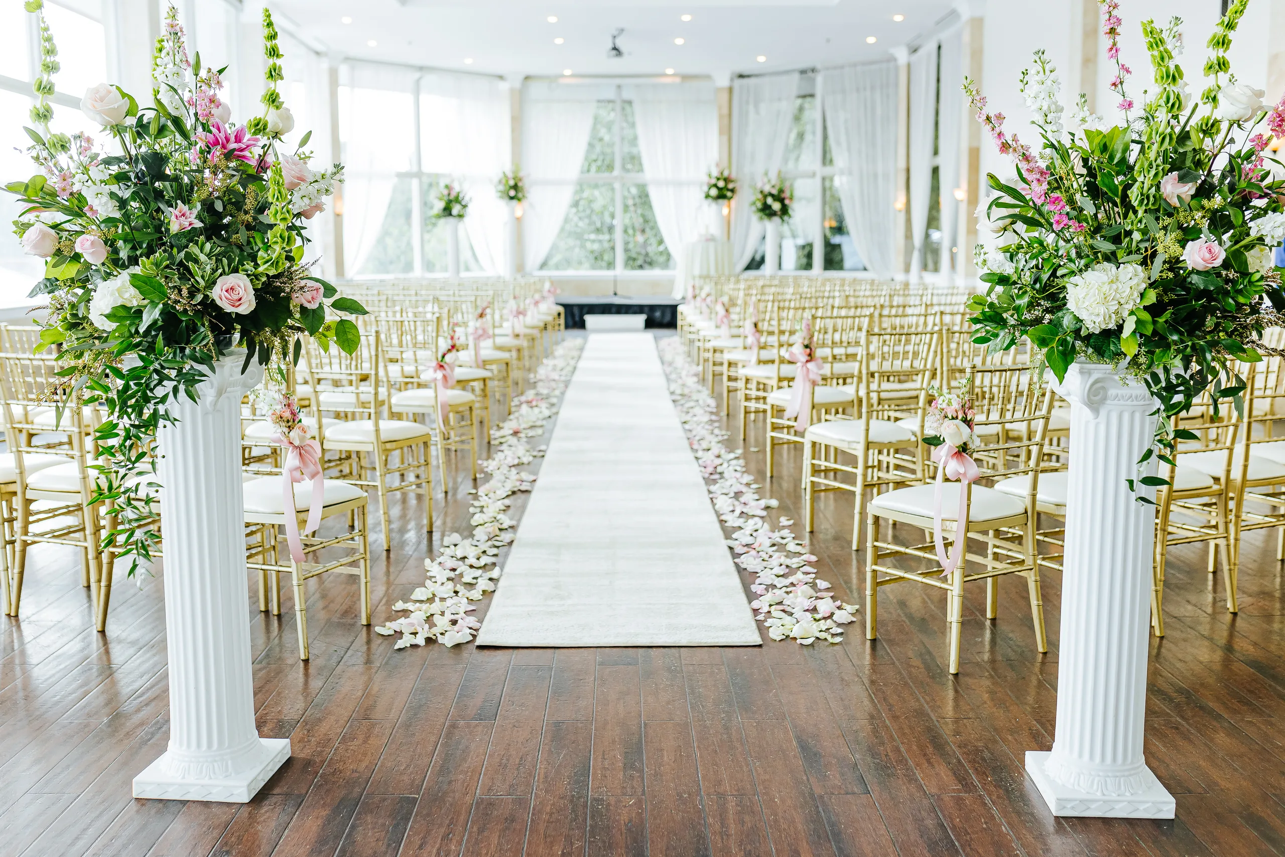 Wedding Ceremony: the aisle lined with petals between gold chairs, arrangements on white columns, at a wedding at The Piedmont Room in Atlanta, GA
