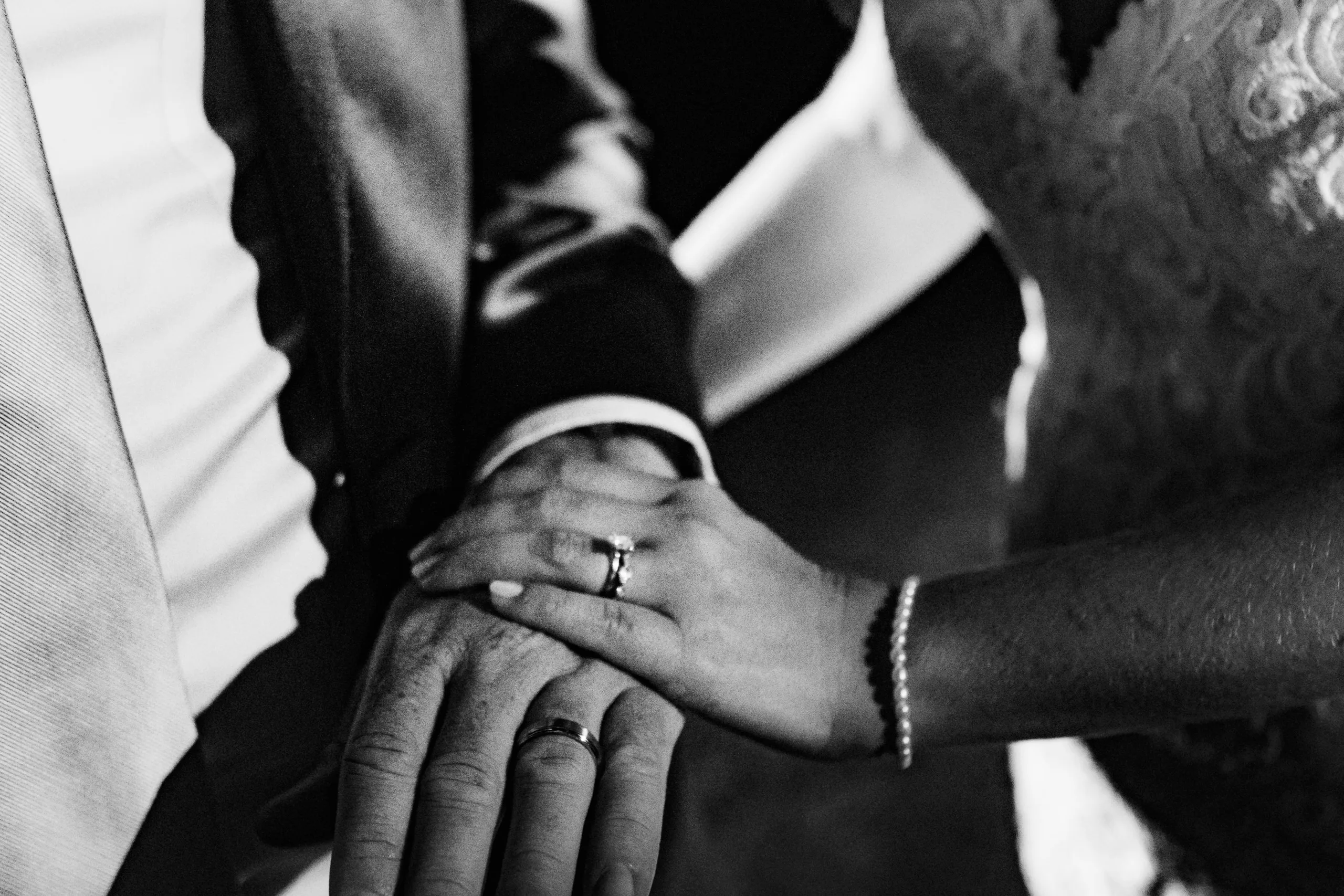 Wedding Ceremony: her hand over his, both rings on, in black and white, at their wedding at The Piedmont Room in Atlanta, GA