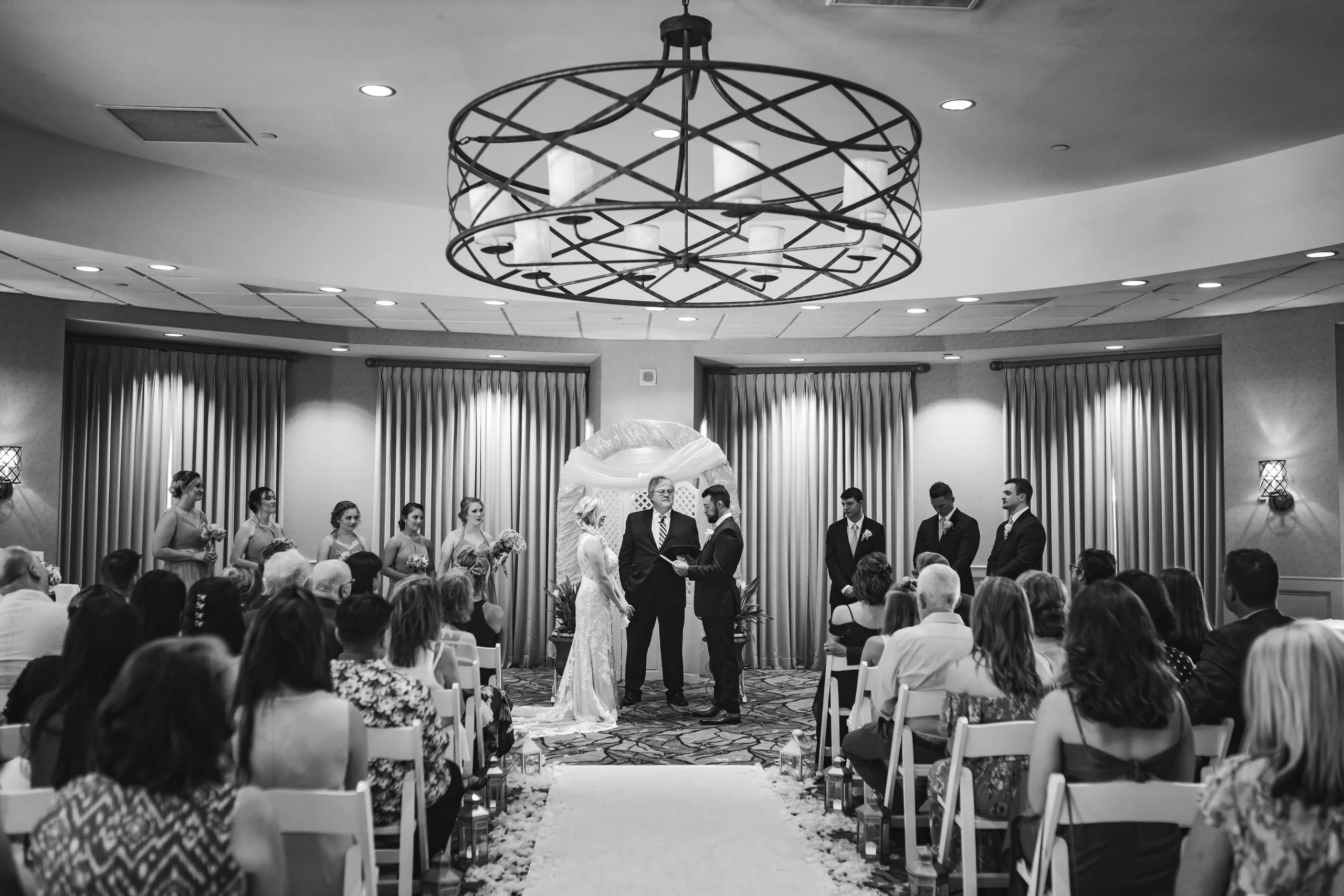 Wedding Ceremony: the ceremony under the chandelier in the ballroom, in black and white, at their wedding at Atlanta Evergreen Lakeside Resort in Stone Mountain, GA