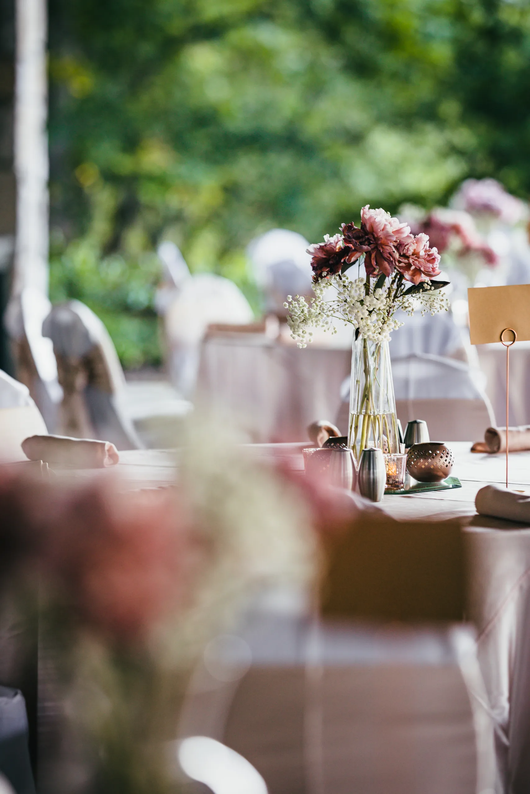 Reception Details: a table set with blush linens and flowers under the pavilion, at a wedding at Atlanta Evergreen Lakeside Resort in Stone Mountain, GA