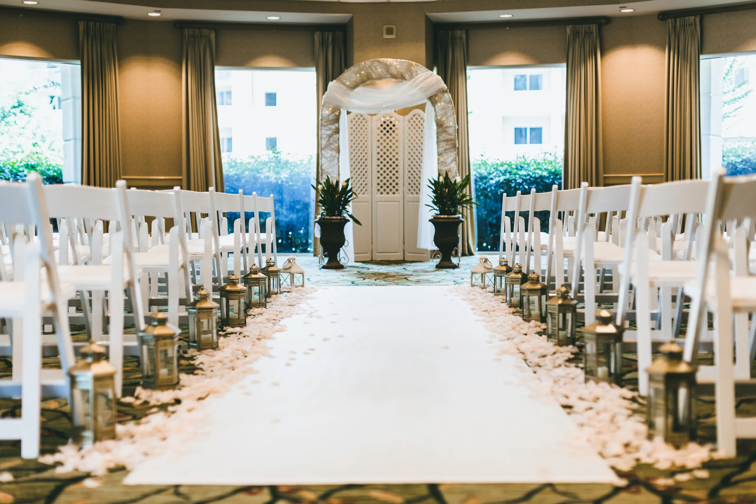 Wedding Ceremony: the aisle lined with petals and lanterns in front of a white arch, at a wedding at Atlanta Evergreen Lakeside Resort in Stone Mountain, GA