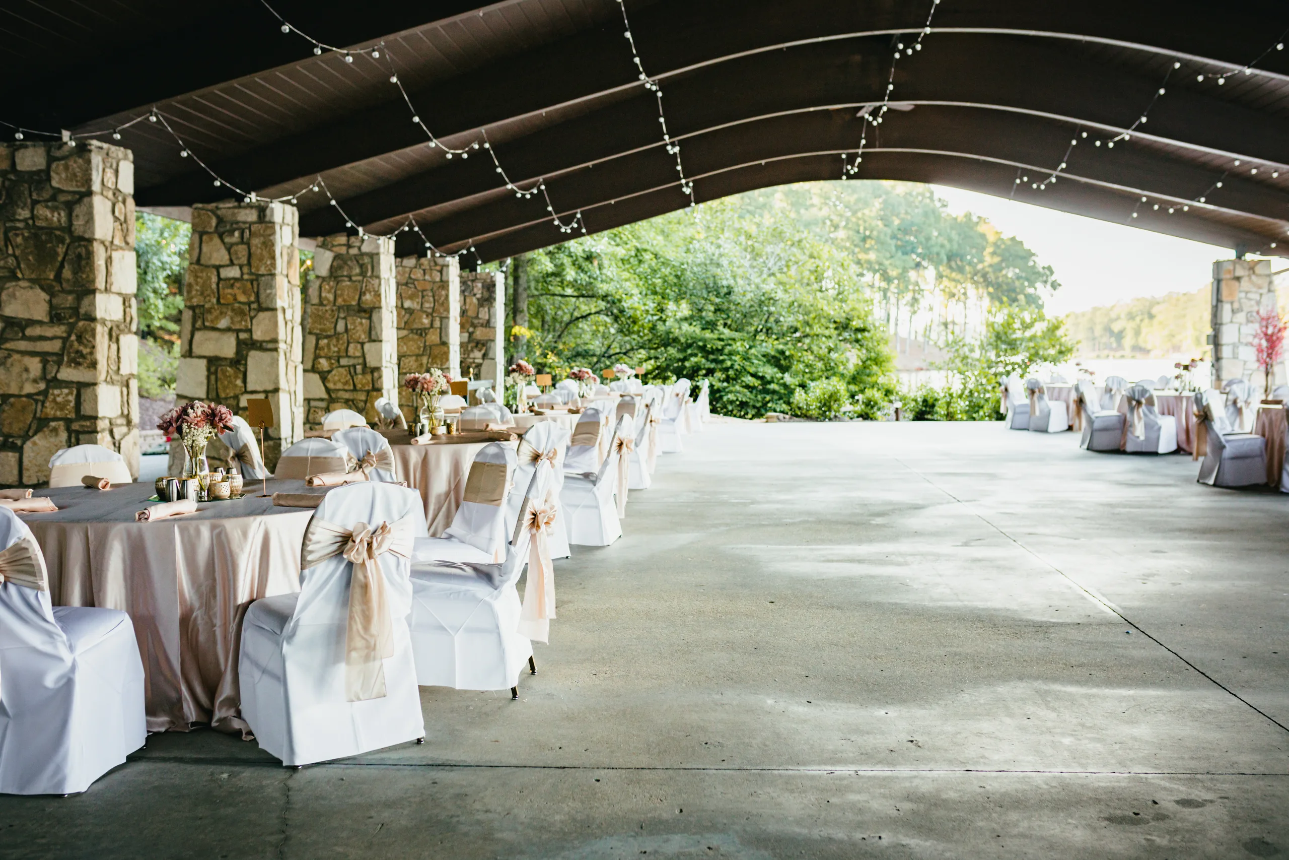 Reception Details: the stone pavilion set with blush tables and string lights, at a wedding at Atlanta Evergreen Lakeside Resort in Stone Mountain, GA