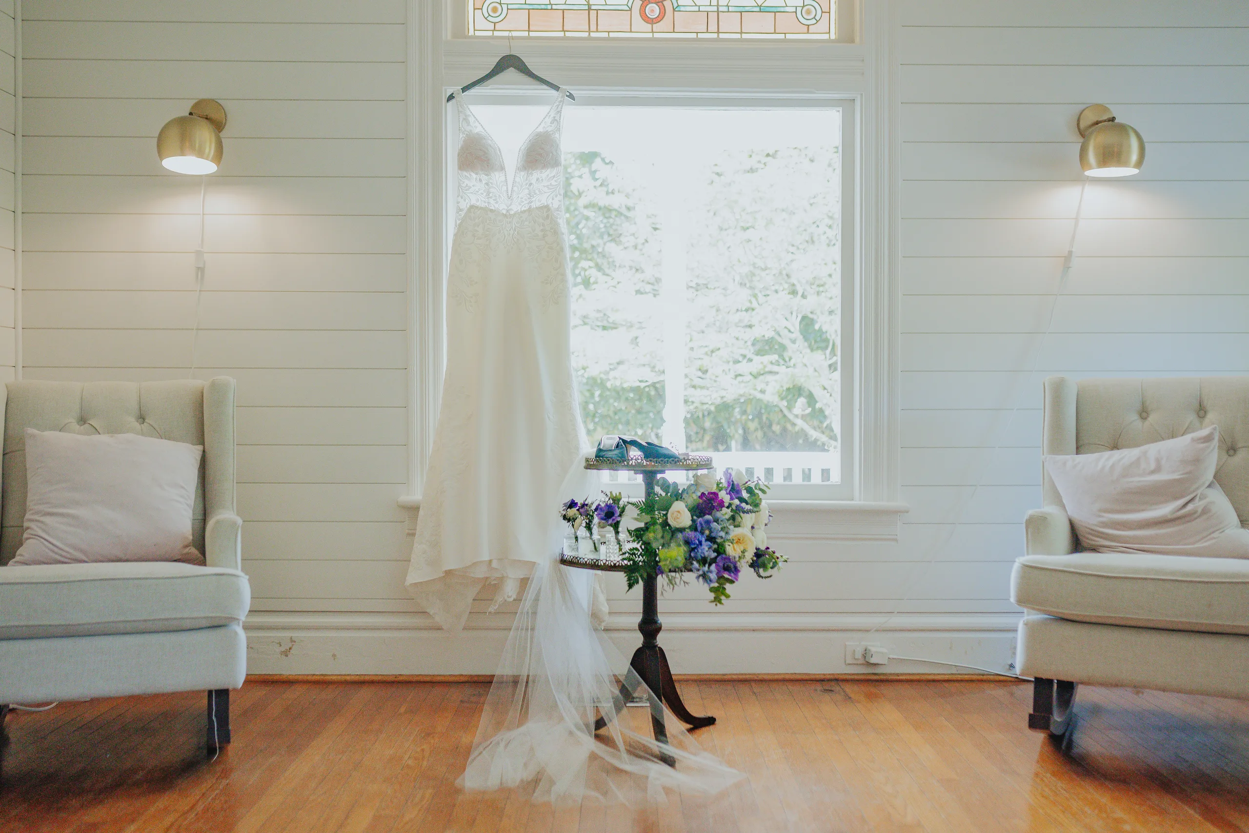 Wedding Details: her gown hanging in the window of the white room, her bouquet on a stand, before their wedding at The Wildflower 301 in Greensboro, GA