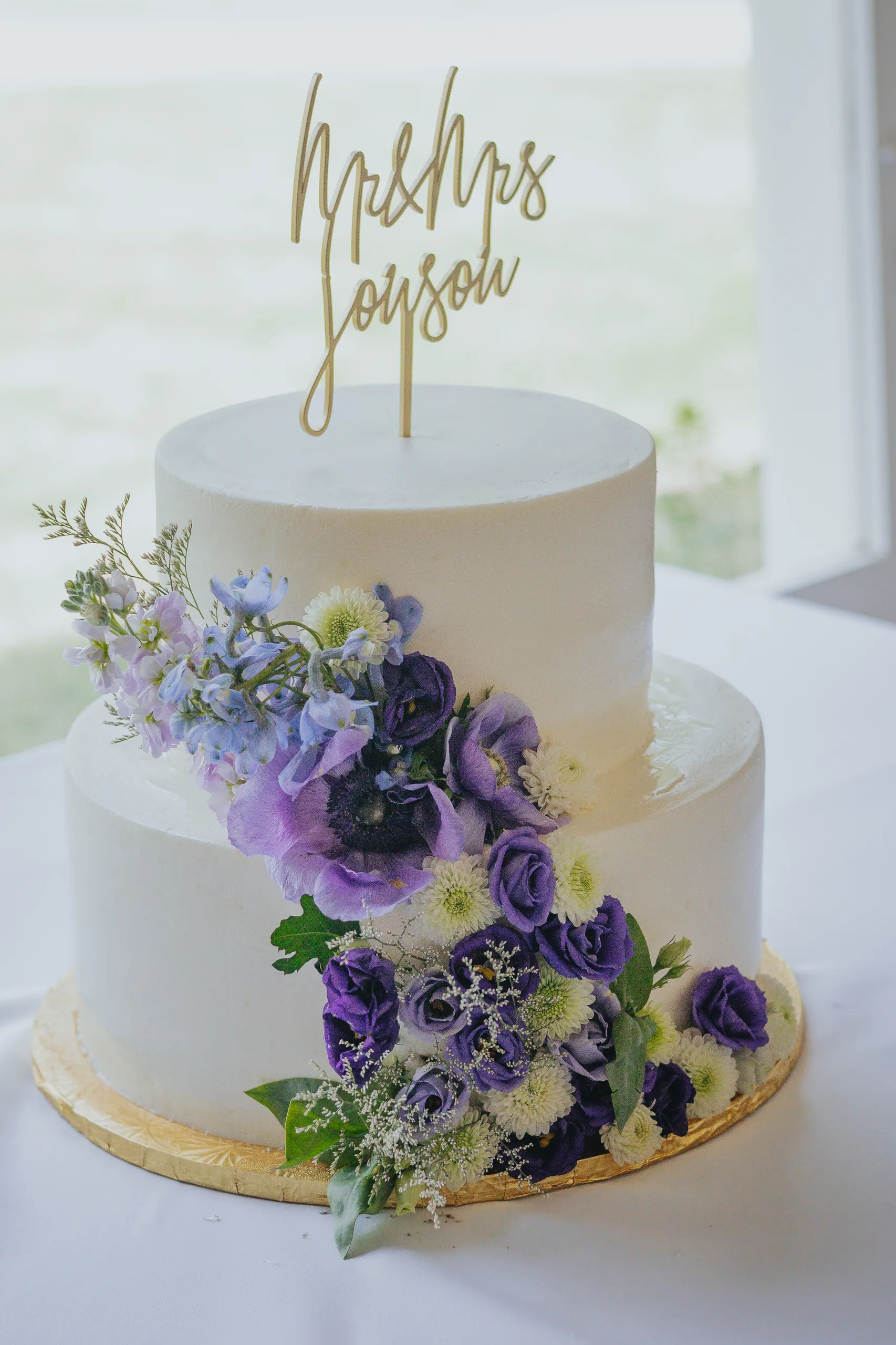 Wedding Cake Details: the two-tier white cake with purple flowers and a gold Mr and Mrs topper, at a wedding at The Wildflower 301 in Greensboro, GA