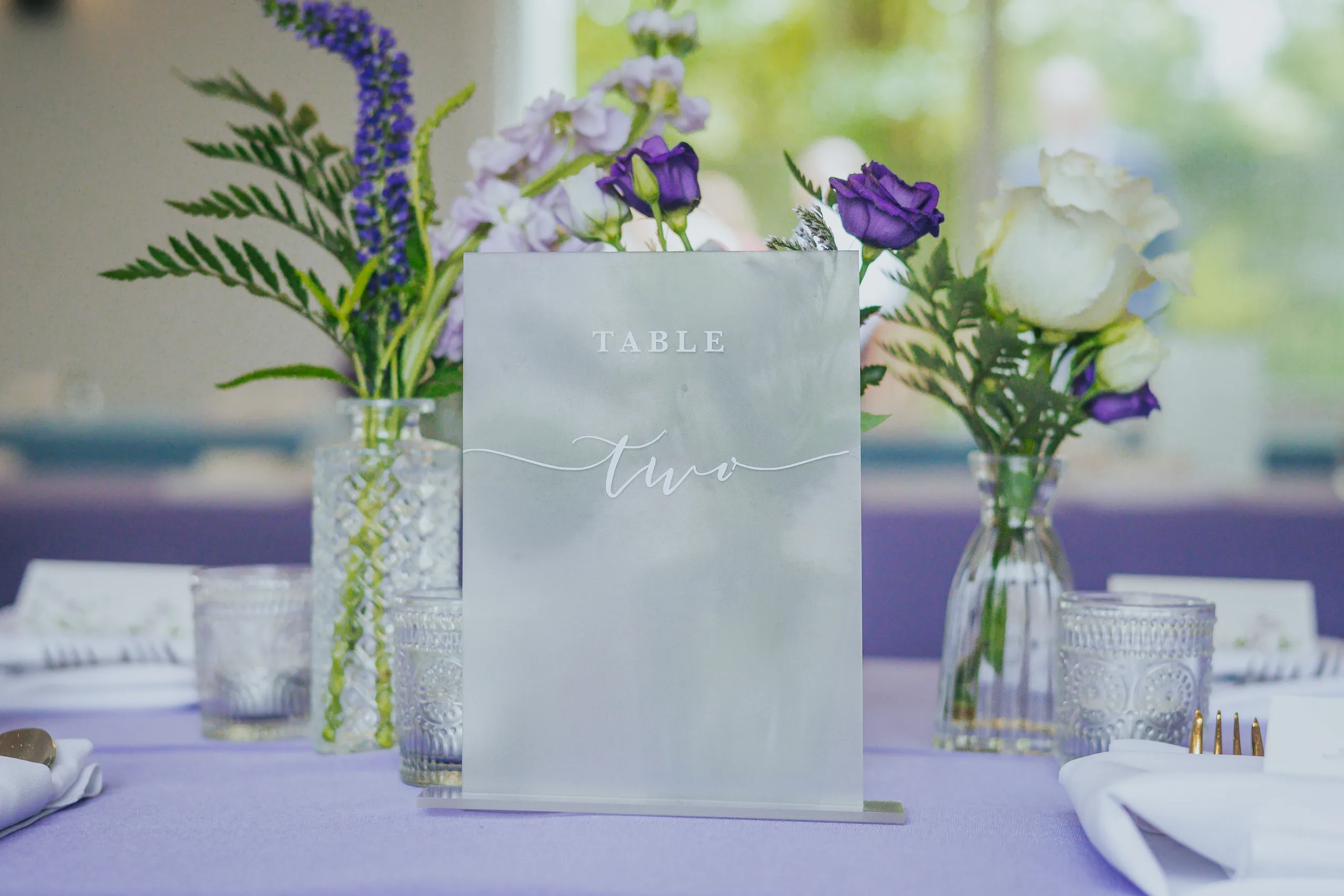 Reception Details: a table number with purple flowers on a lavender tablecloth, at a wedding at The Wildflower 301 in Greensboro, GA
