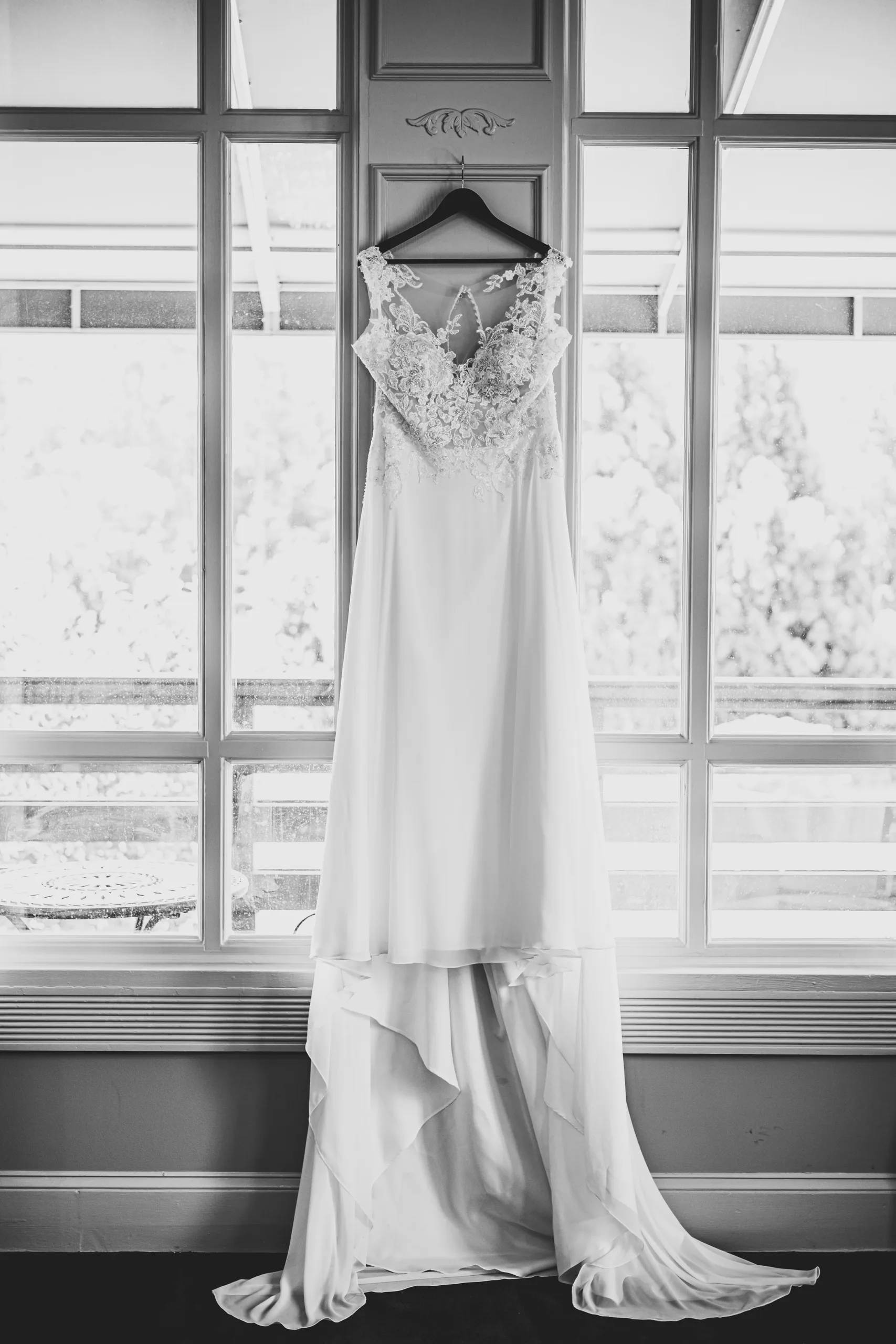 Wedding Details: her lace gown hanging in the window, in black and white before their wedding at the Country Club of Roswell in Roswell, GA