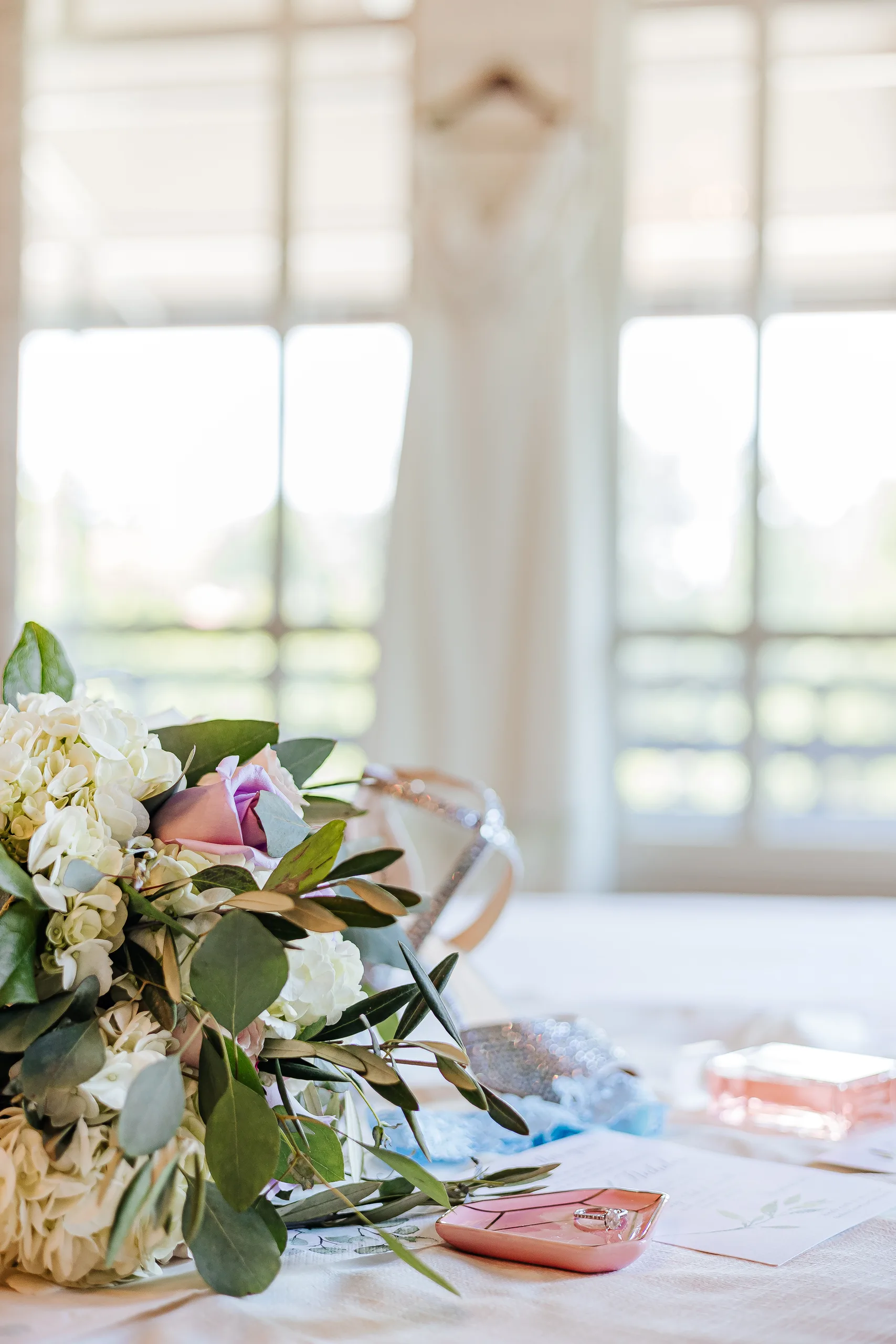 Wedding Florals: her bouquet on the table with her gown hanging behind at a wedding at the Country Club of Roswell in Roswell, GA