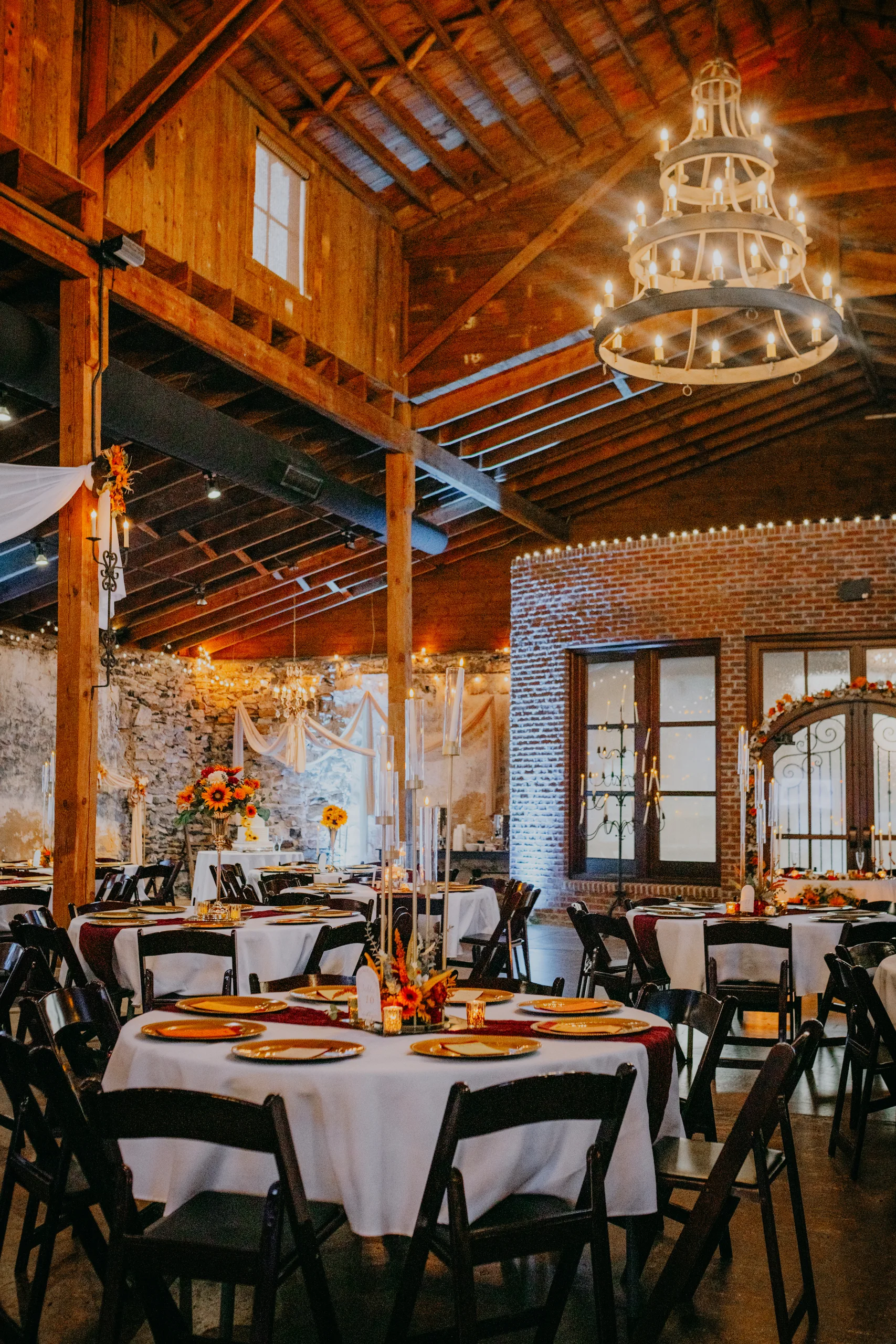Reception Details: tables set with gold chargers under a wagon wheel chandelier, at a wedding at 550 Trackside in Lawrenceville, GA