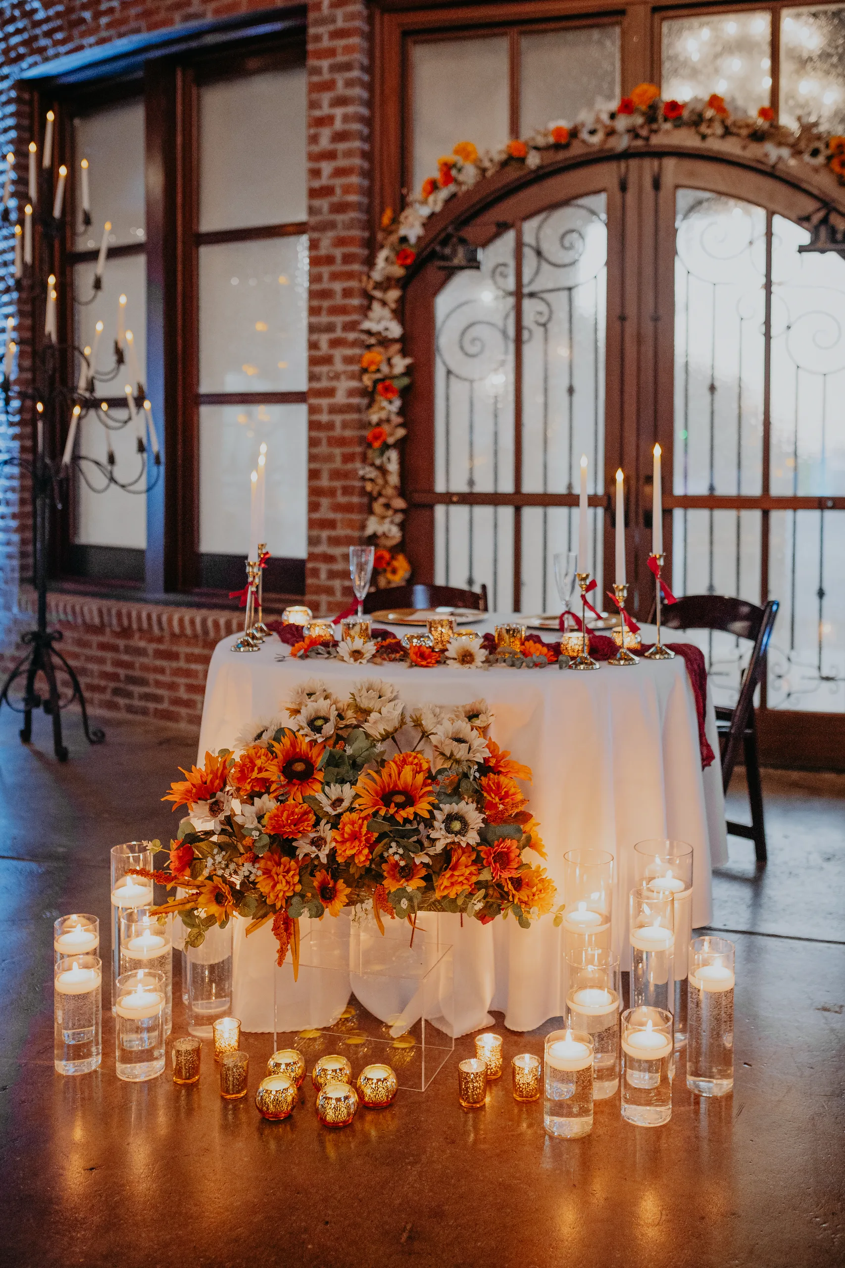 Reception Details: the sweetheart table with sunflowers and candles under a floral arch, at a wedding at 550 Trackside in Lawrenceville, GA