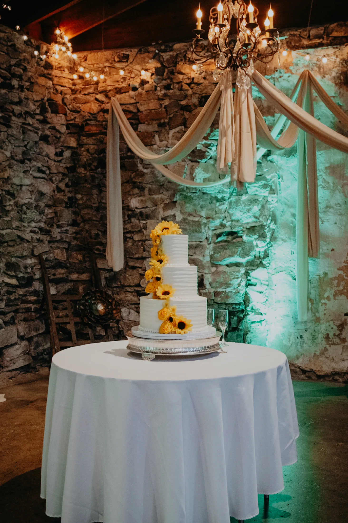 Wedding Cake Details: the white cake with sunflowers against the stone wall, at a wedding at 550 Trackside in Lawrenceville, GA