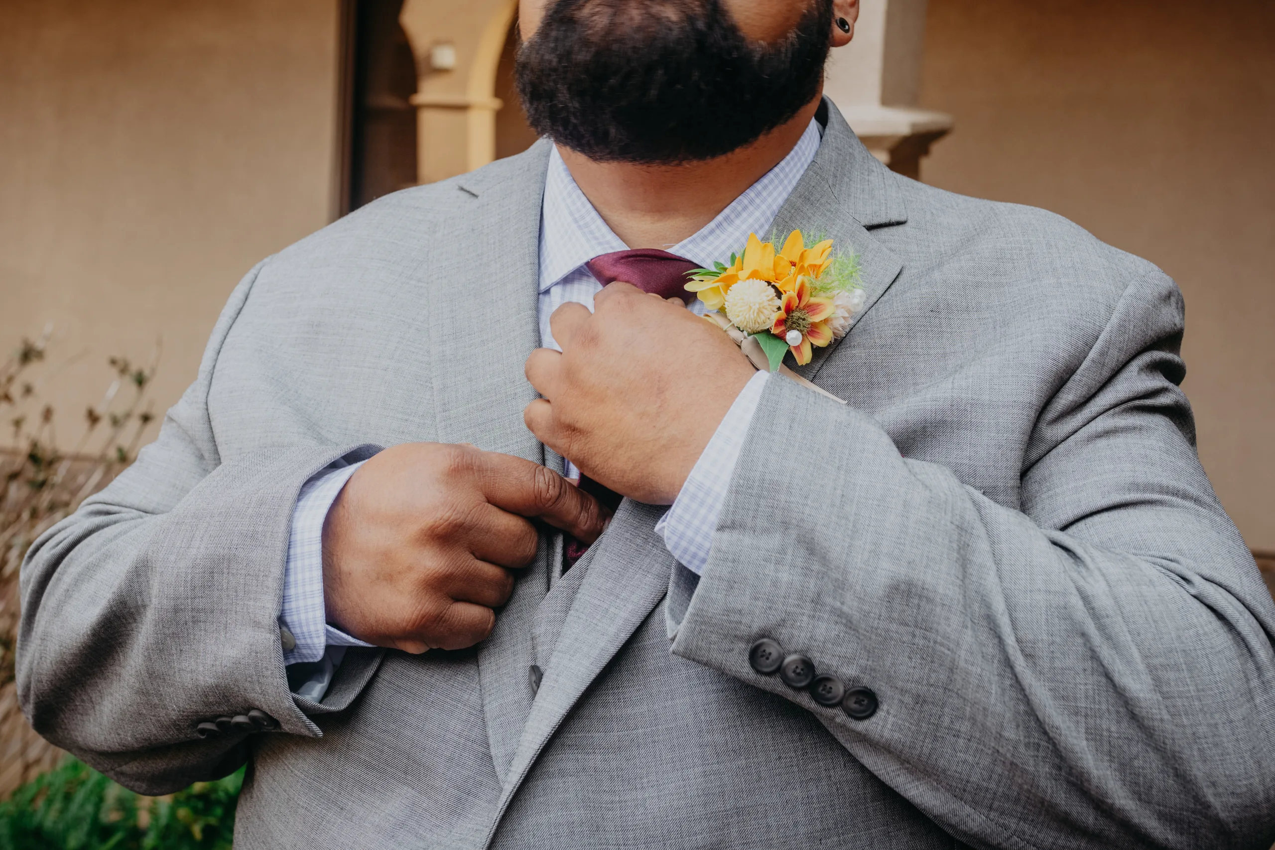 Wedding Details: the groom fixing his burgundy tie, a sunflower boutonniere on his lapel, at their wedding at St. Lawrence Catholic Church in Lawrenceville, GA