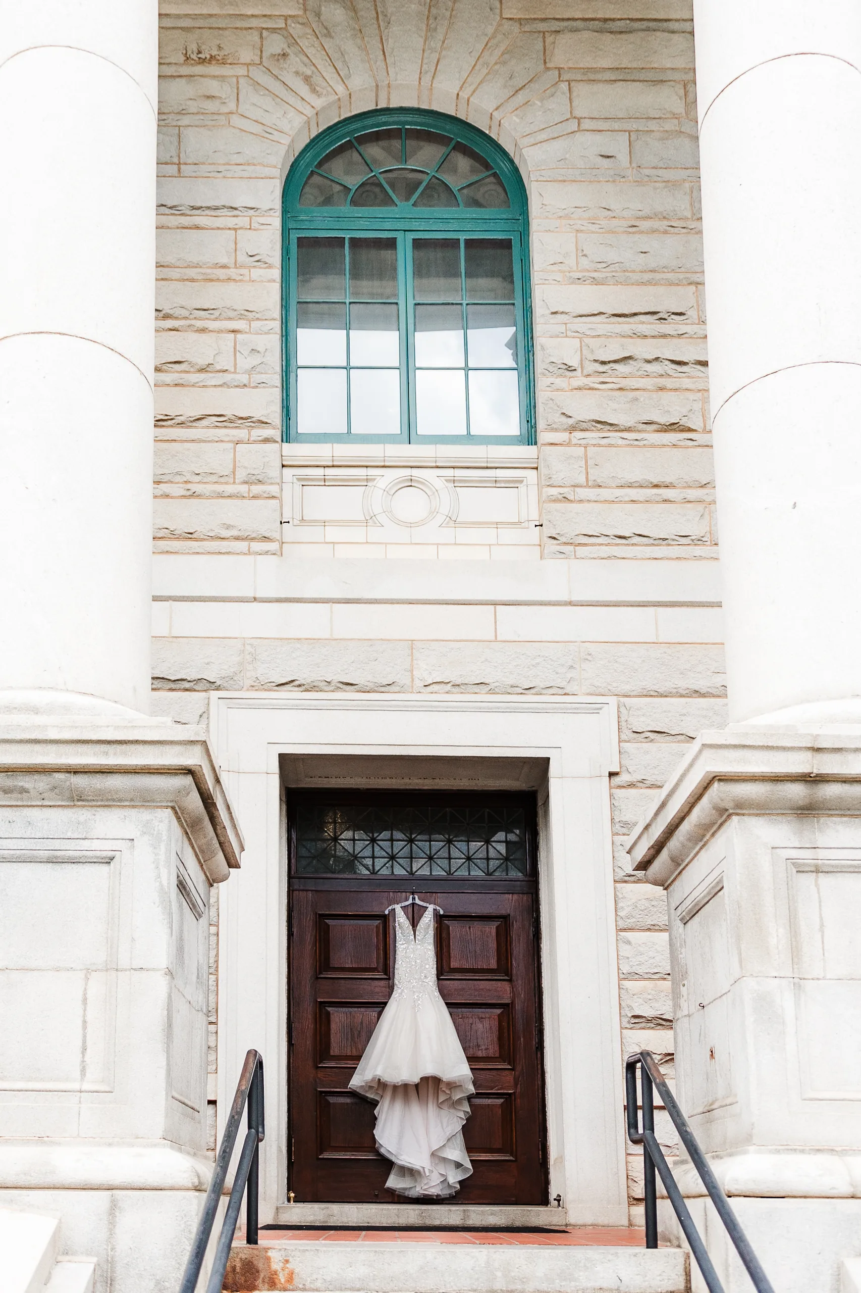 Wedding Details: her gown on the front doors under the arched green window and stone columns, at a wedding at the Historic DeKalb Courthouse in Decatur, GA