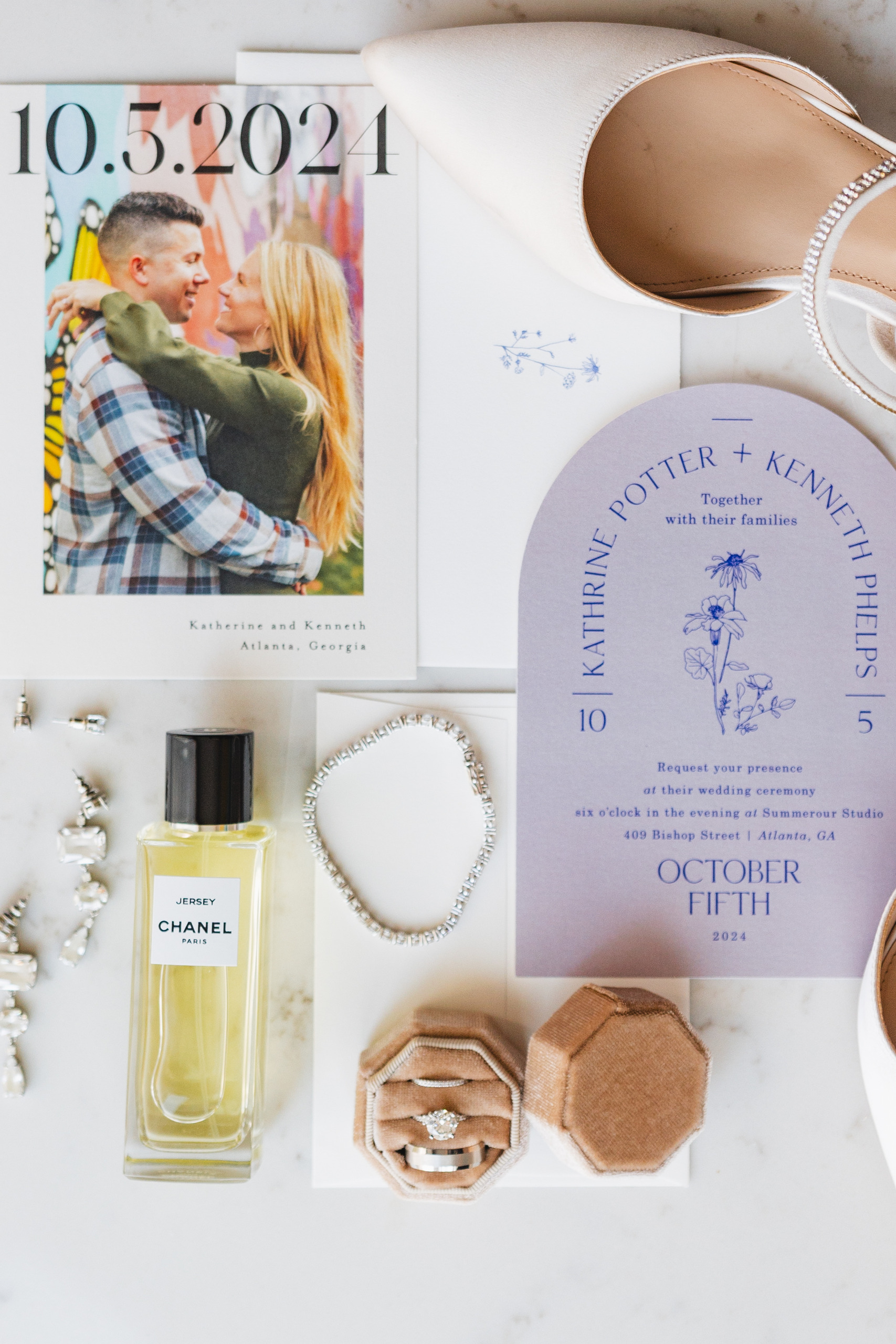 Wedding Details: the lavender arched invitation suite, her perfume, crystal earrings and satin heels, at a wedding at Summerour Studio in Atlanta, GA