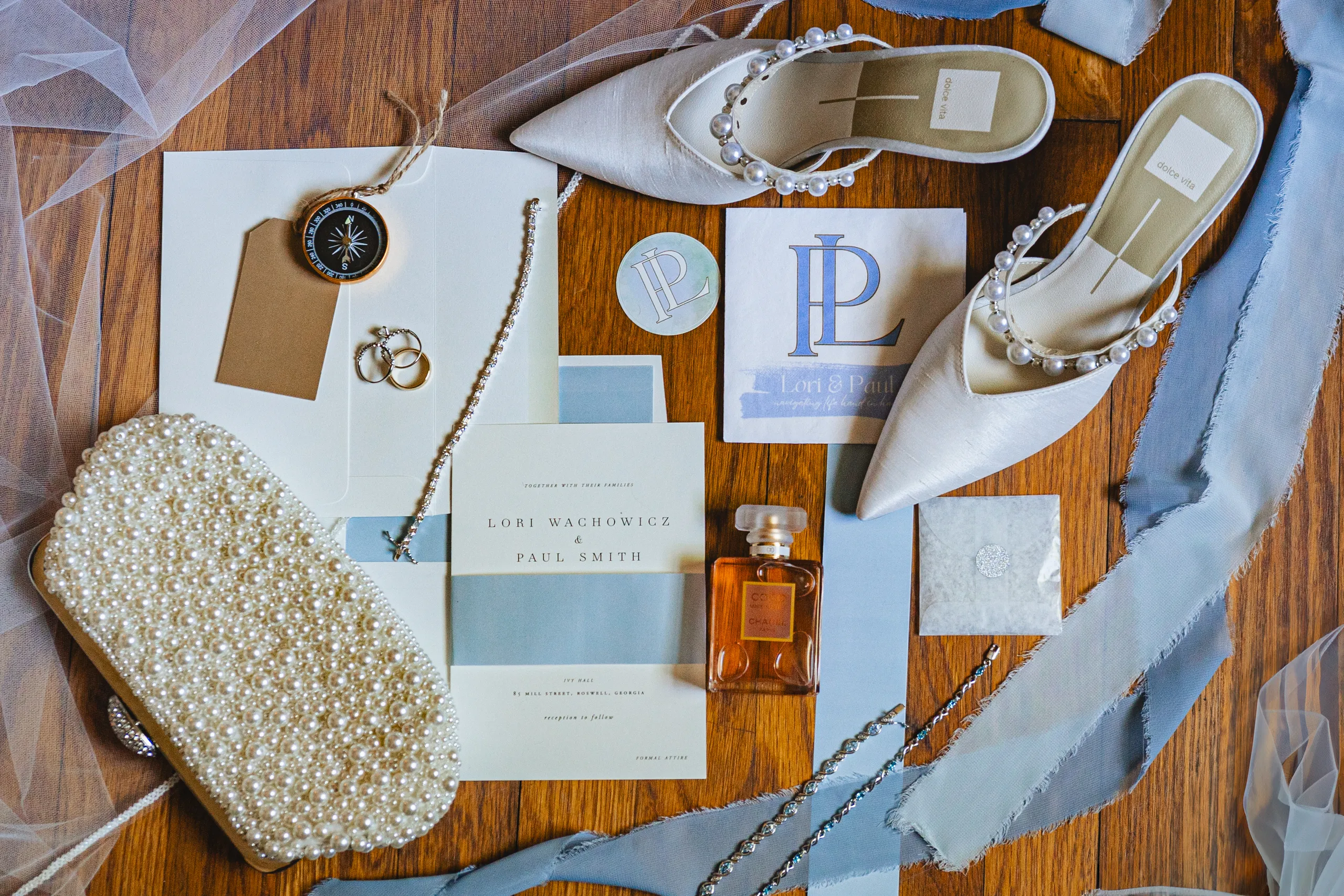 Wedding Details: the invitation suite, pearl heels, clutch and compass on the floor at a wedding at Ivy Hall at Roswell Mill in Roswell, GA