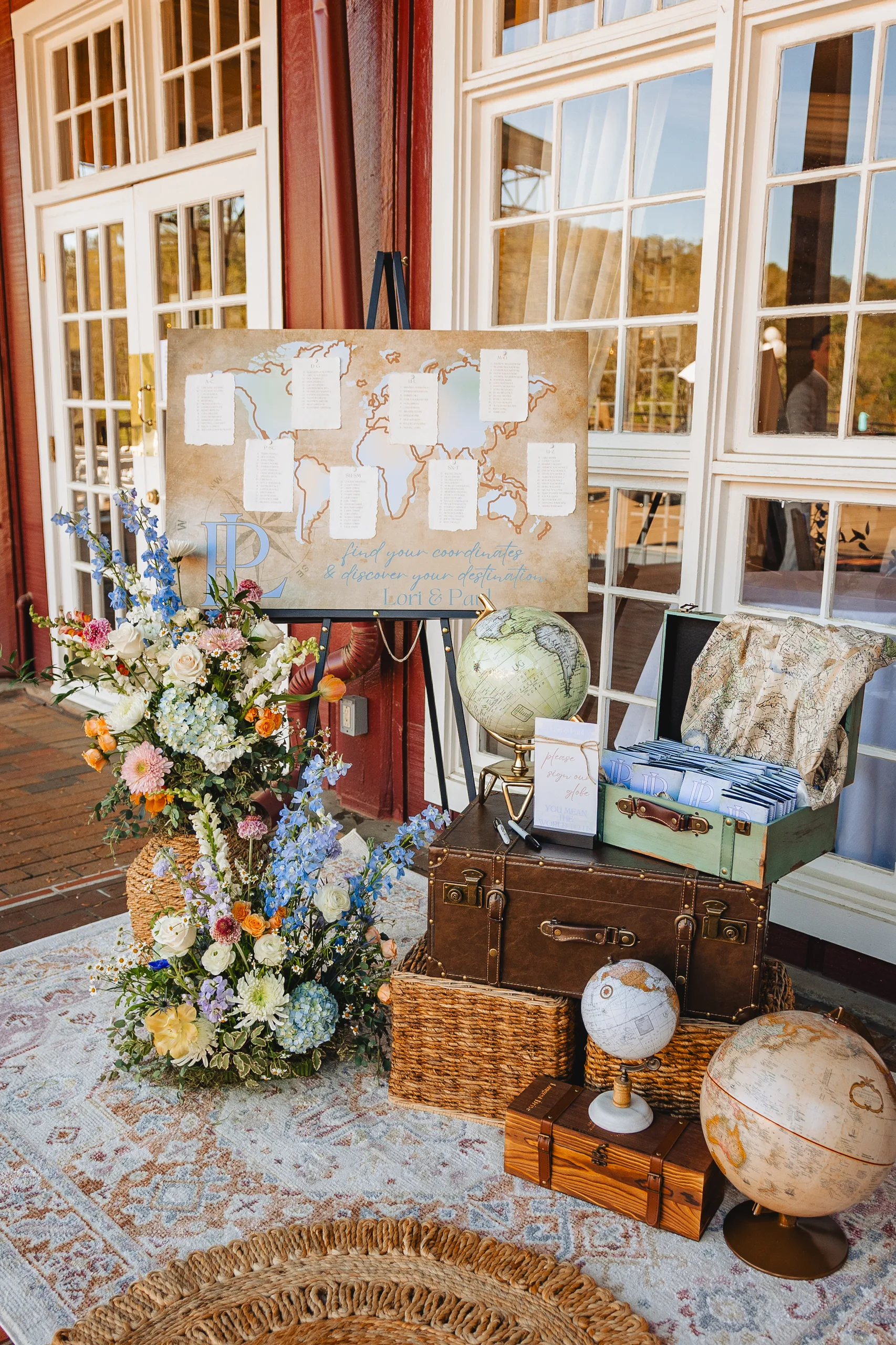 Reception Details: the map seating chart with vintage suitcases, globes and flowers at a wedding at Ivy Hall at Roswell Mill in Roswell, GA