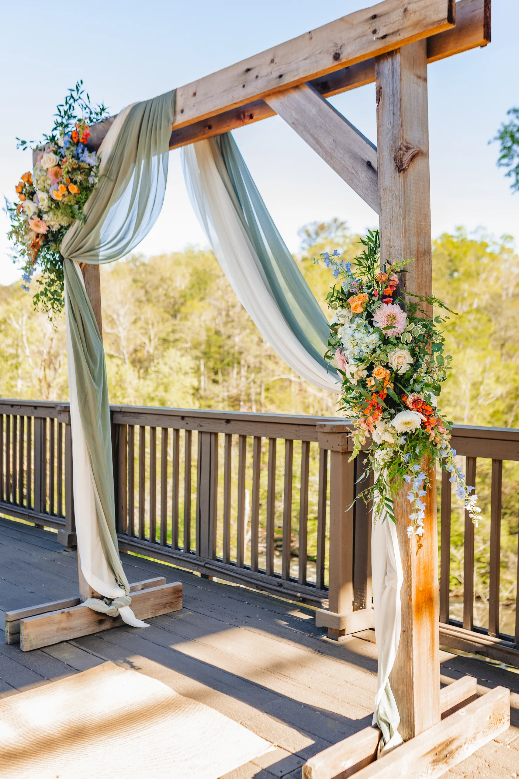 Wedding Ceremony: the wooden arch draped in sage fabric with flowers on the deck at a wedding at Ivy Hall at Roswell Mill in Roswell, GA