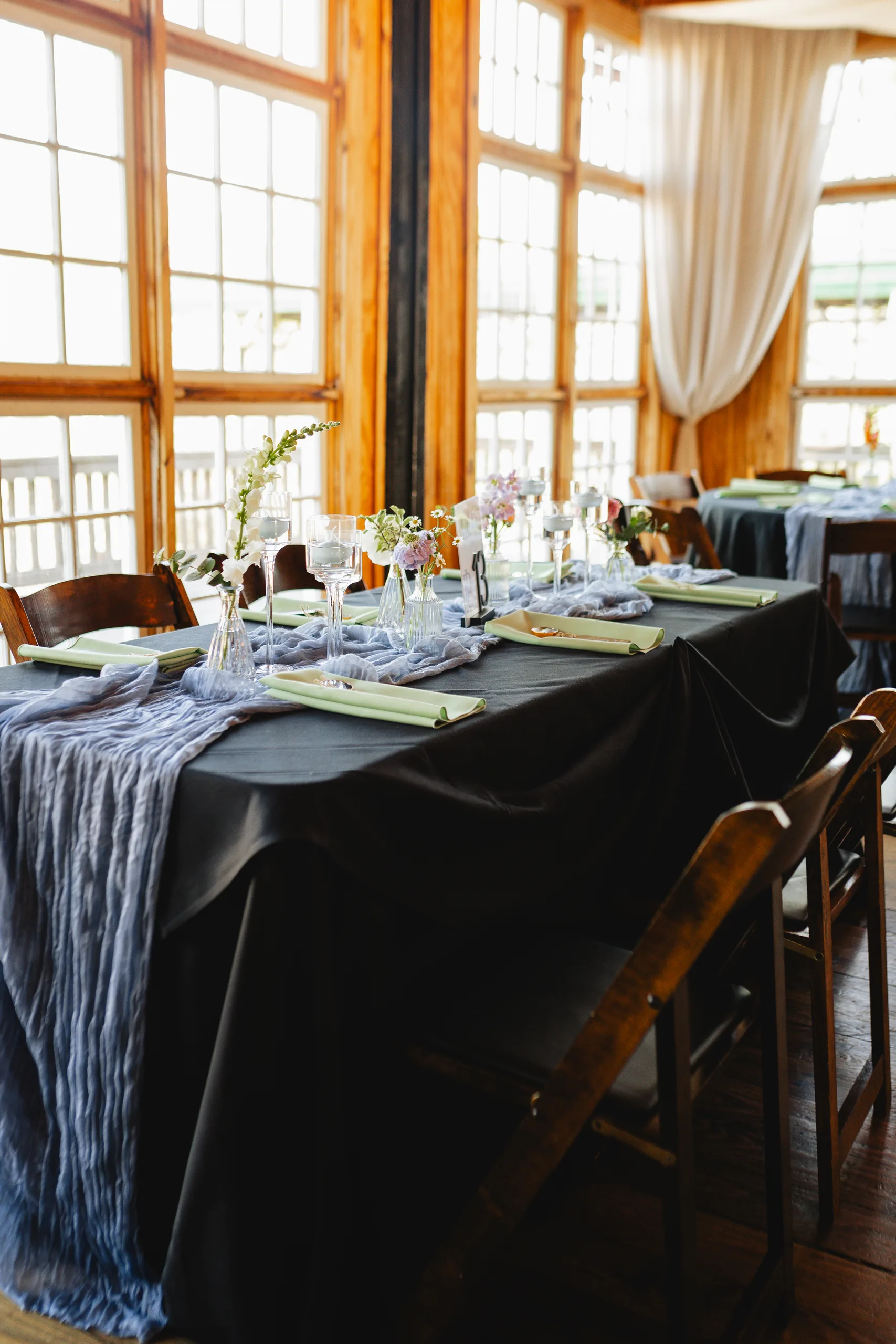 Reception Details: a long table by the tall windows at a wedding at Ivy Hall at Roswell Mill in Roswell, GA