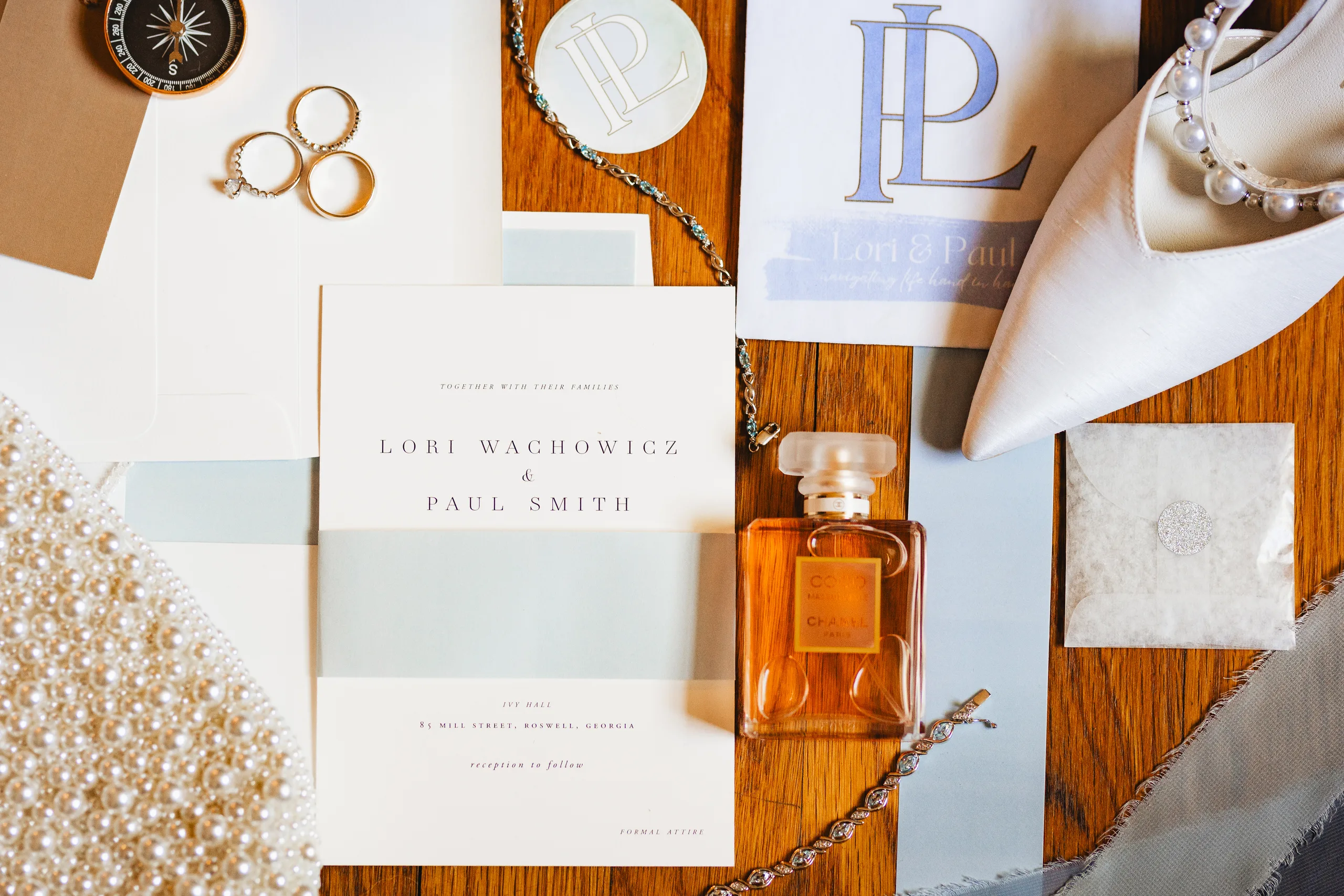 Wedding Details: the invitation suite with a compass, rings, perfume, pearl clutch and heels at a wedding at Ivy Hall at Roswell Mill in Roswell, GA