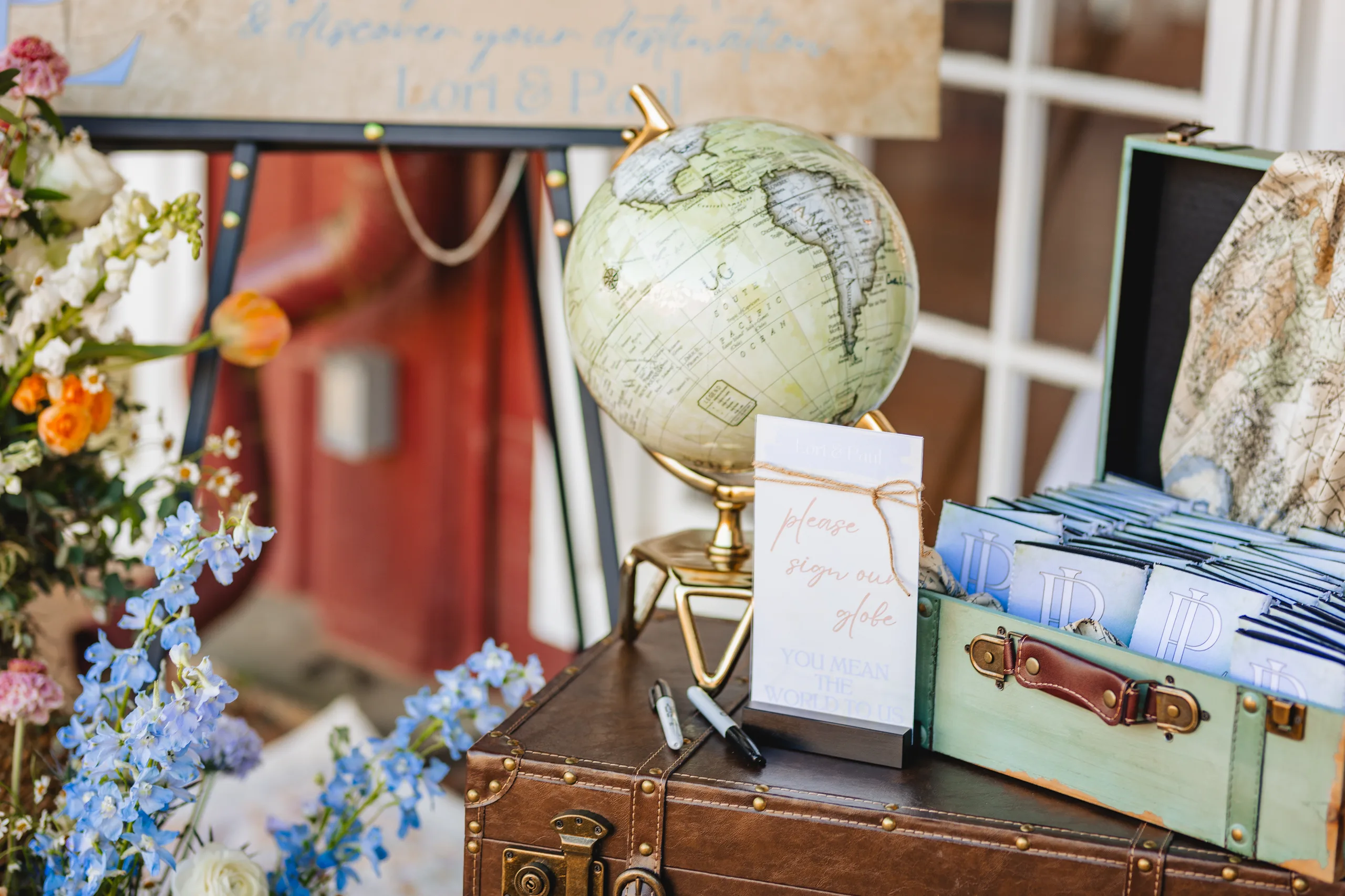 Reception Details: a globe and a vintage suitcase full of monogrammed koozies at a wedding at Ivy Hall at Roswell Mill in Roswell, GA