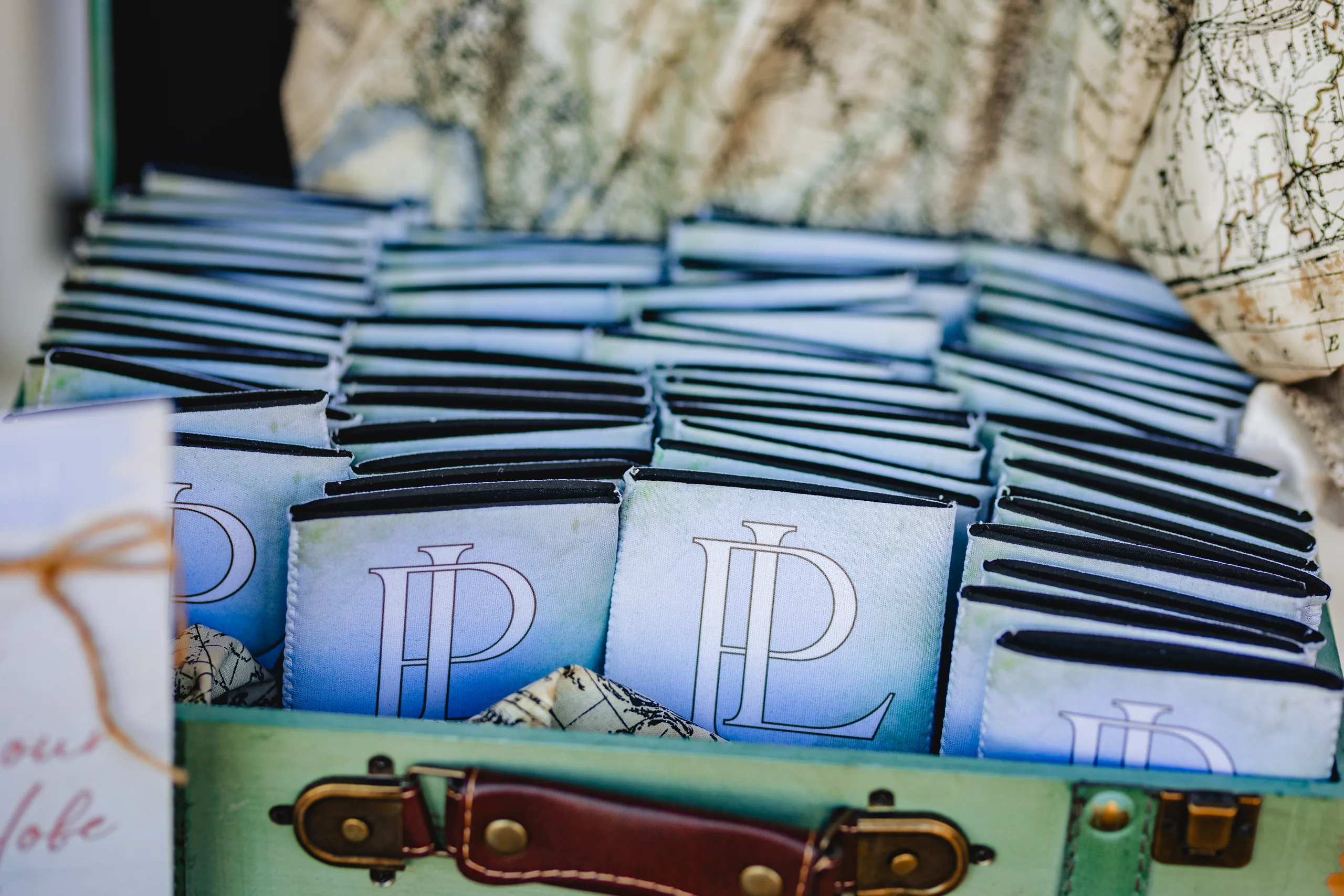 Reception Details: monogrammed koozies packed in a vintage suitcase at a wedding at Ivy Hall at Roswell Mill in Roswell, GA