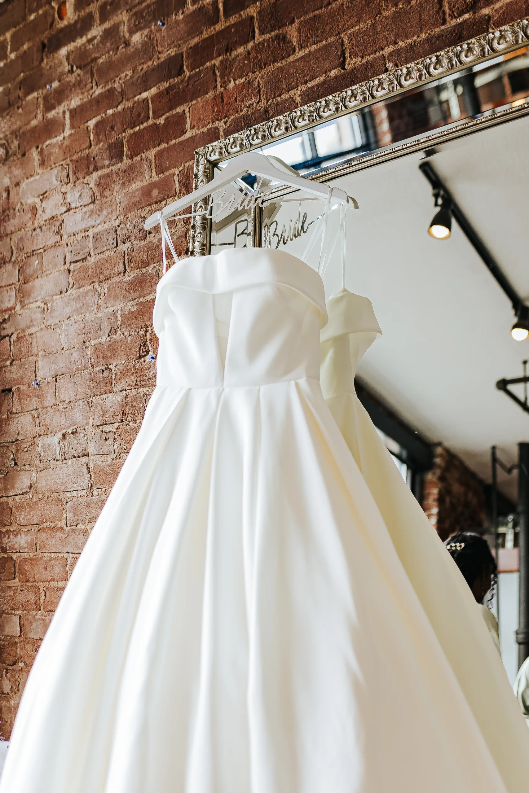 Wedding Details: her strapless satin gown hanging against the brick wall, at a wedding at Terminus 330 in Atlanta, GA