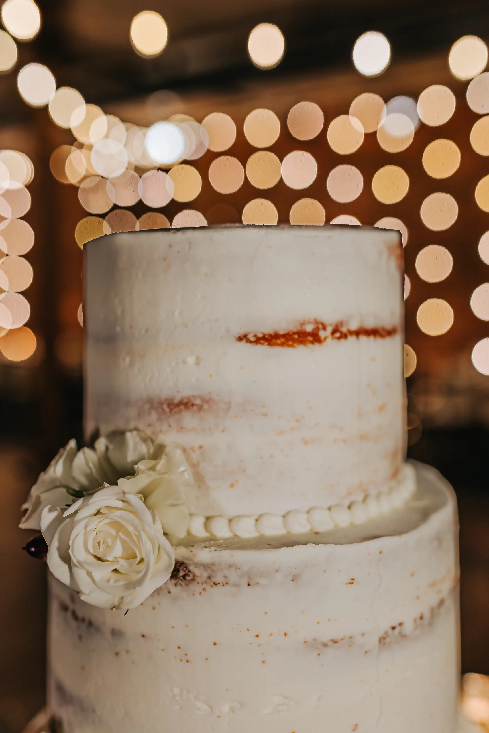 Wedding Cake Details: the top of the cake with white roses and string lights behind, at a wedding at Terminus 330 in Atlanta, GA