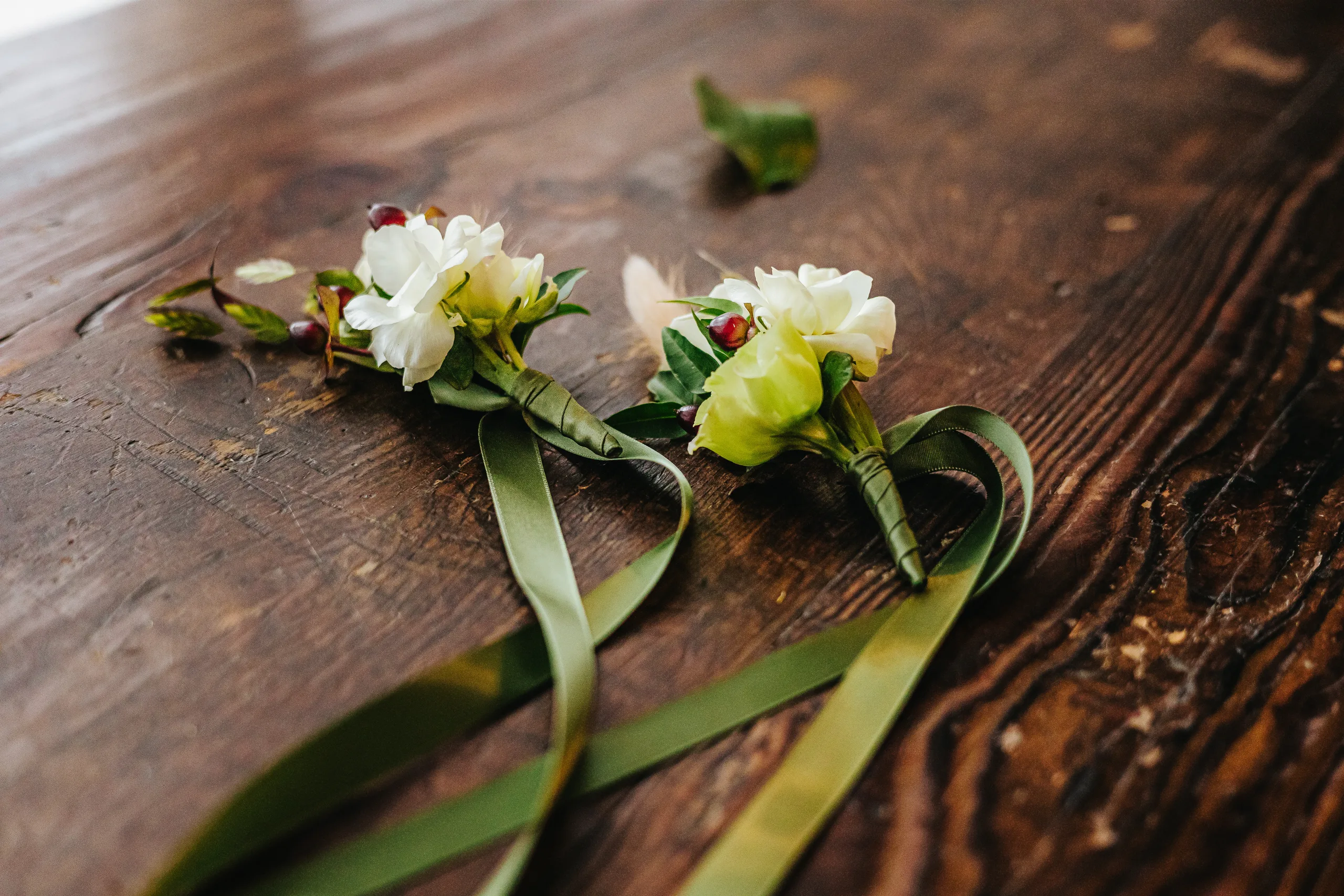 Wedding Details: two white boutonnieres with green ribbon on a wooden table, at a wedding at Terminus 330 in Atlanta, GA