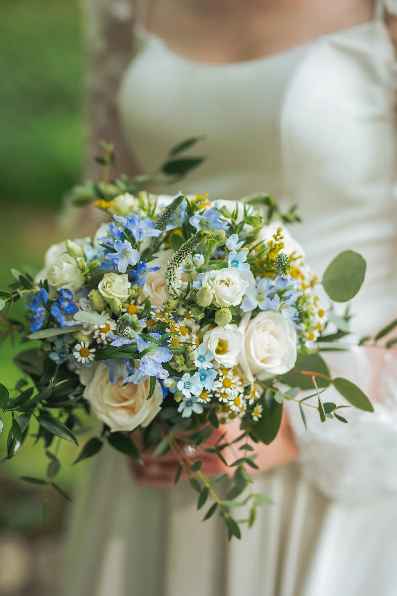 Wedding Florals: her bouquet of white roses, blue delphinium and yellow flowers, at a wedding at Cator Woolford Gardens in Atlanta, GA