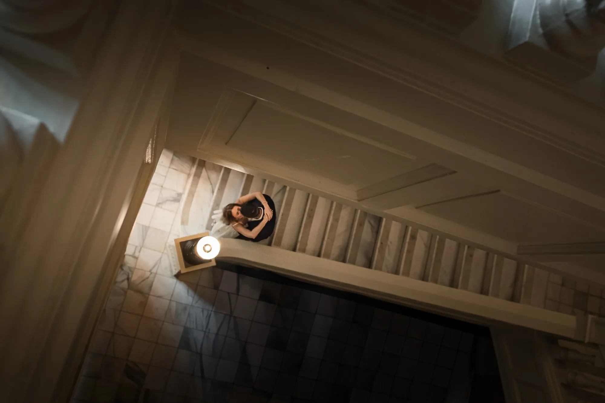 Grand Staircase: looking straight down the stairwell at the two of them embracing beside a lamp, at their engagement session at the Georgia State Capitol in Atlanta, GA