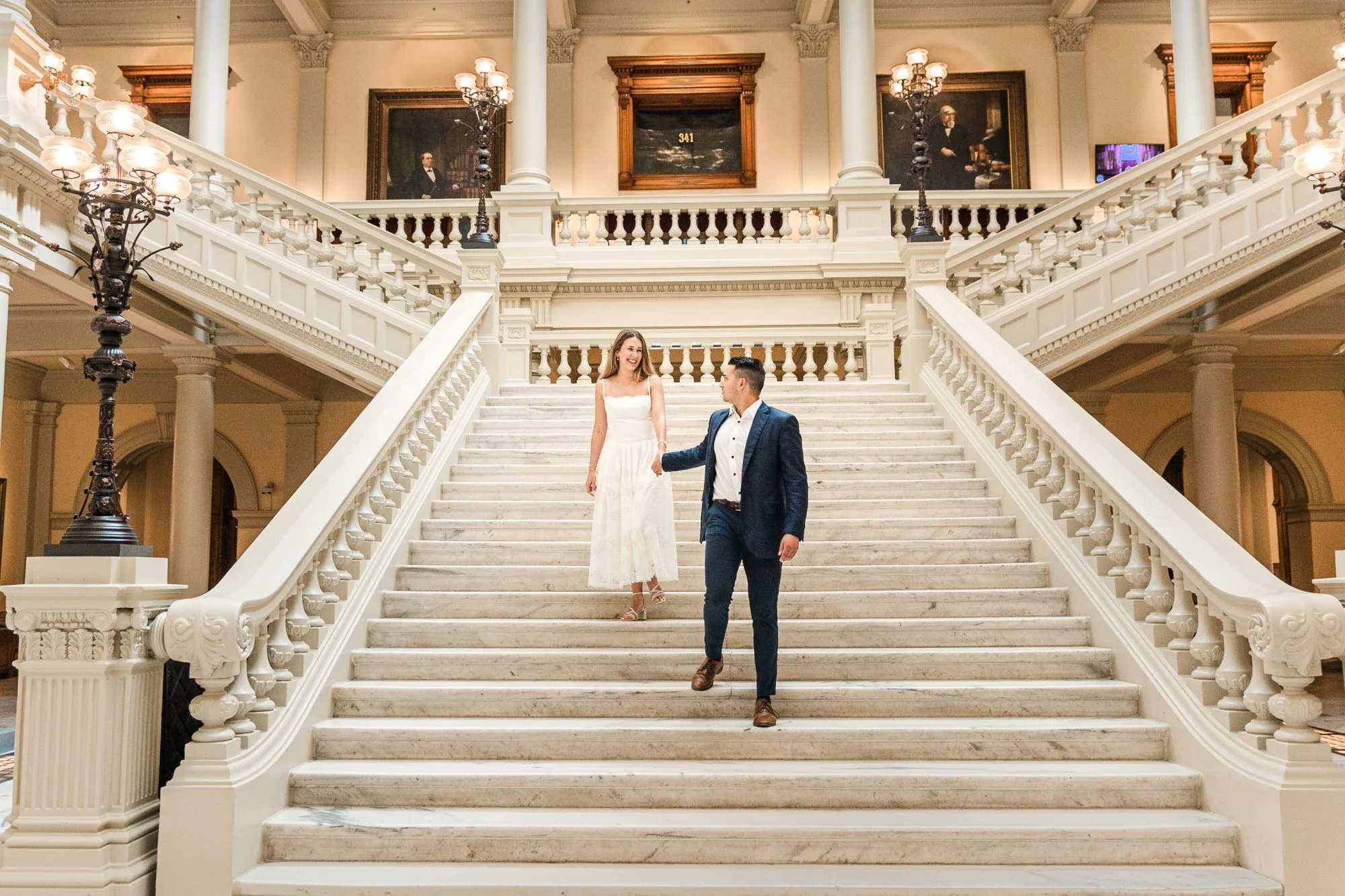 Grand Staircase: him leading her down the marble staircase by the hand, at their engagement session at the Georgia State Capitol in Atlanta, GA