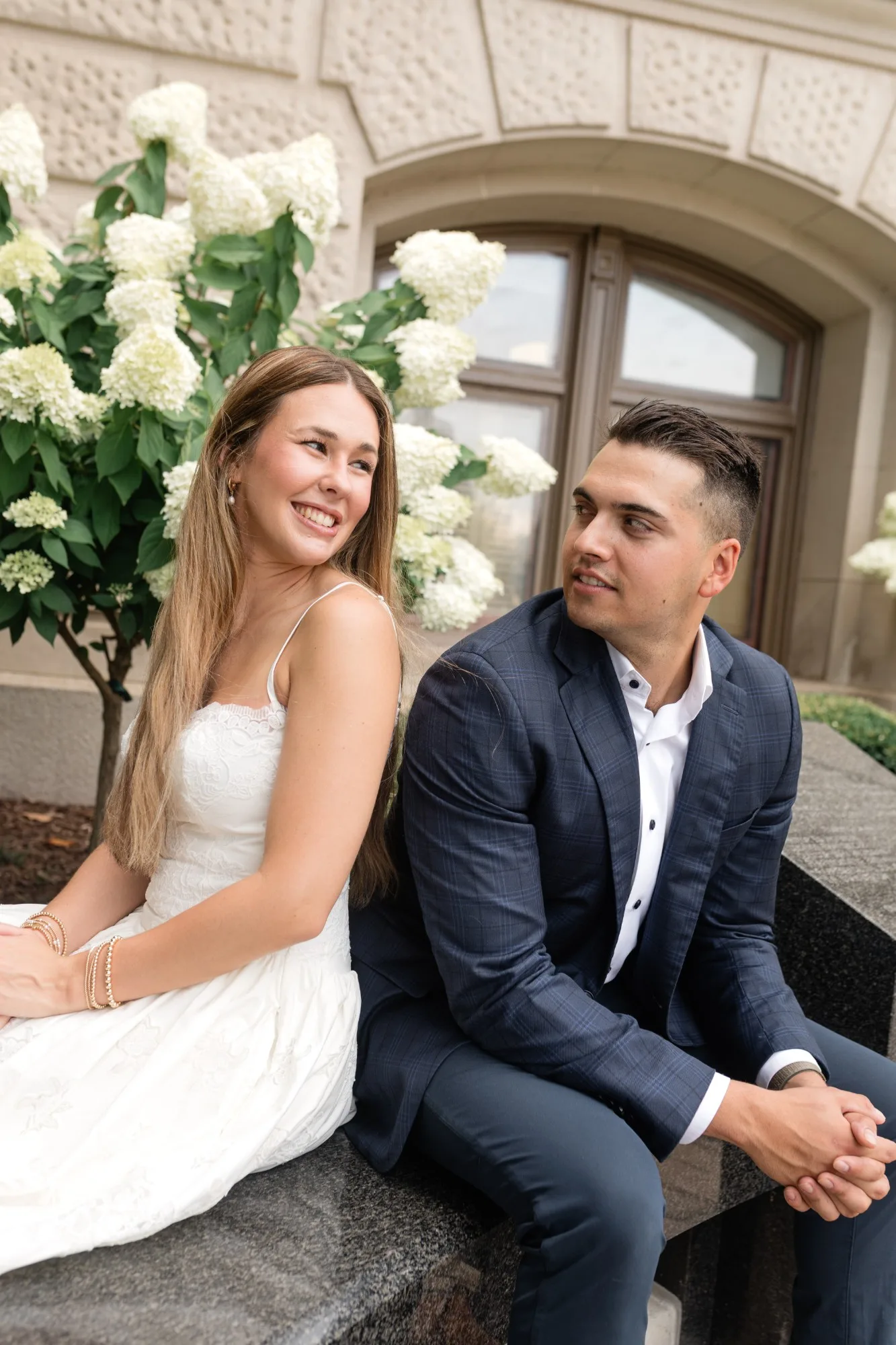Capitol Grounds: back to back on the bench, looking over their shoulders, an arched window behind, at their engagement session at the Georgia State Capitol in Atlanta, GA