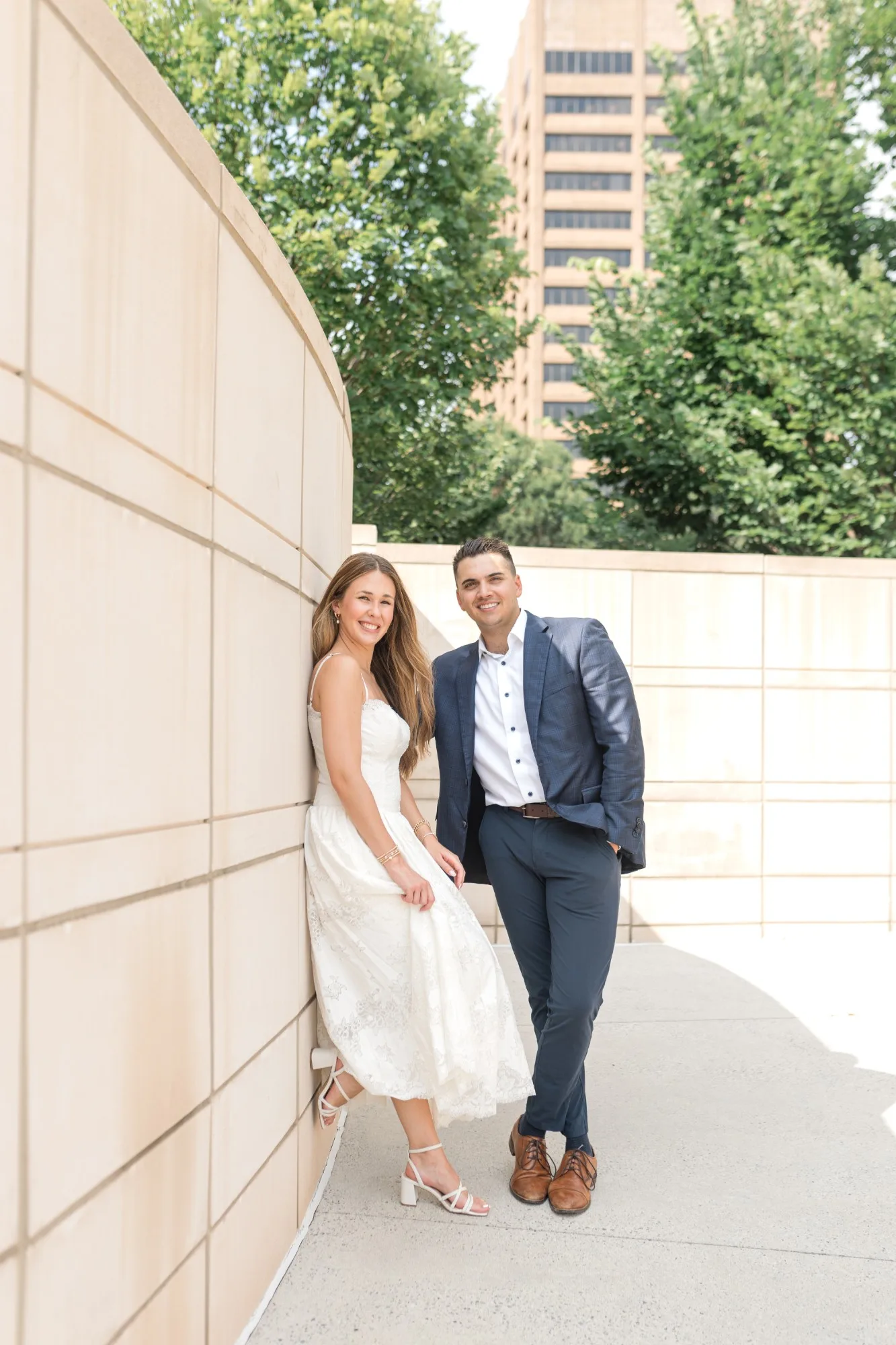 Capitol Grounds: leaning on a curved limestone wall, a downtown tower behind them, at their engagement session at the Georgia State Capitol in Atlanta, GA
