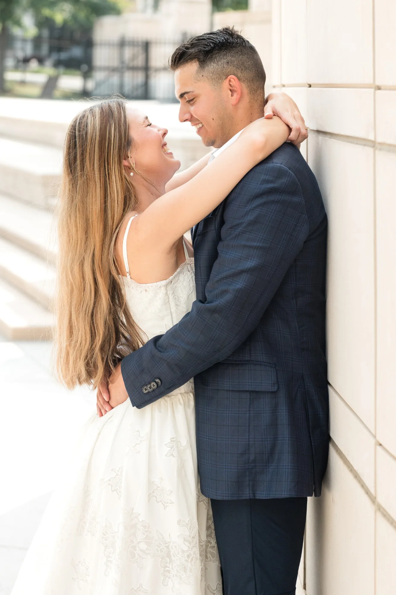 Capitol Grounds: her arms around his neck against the stone wall, laughing, at their engagement session at the Georgia State Capitol in Atlanta, GA