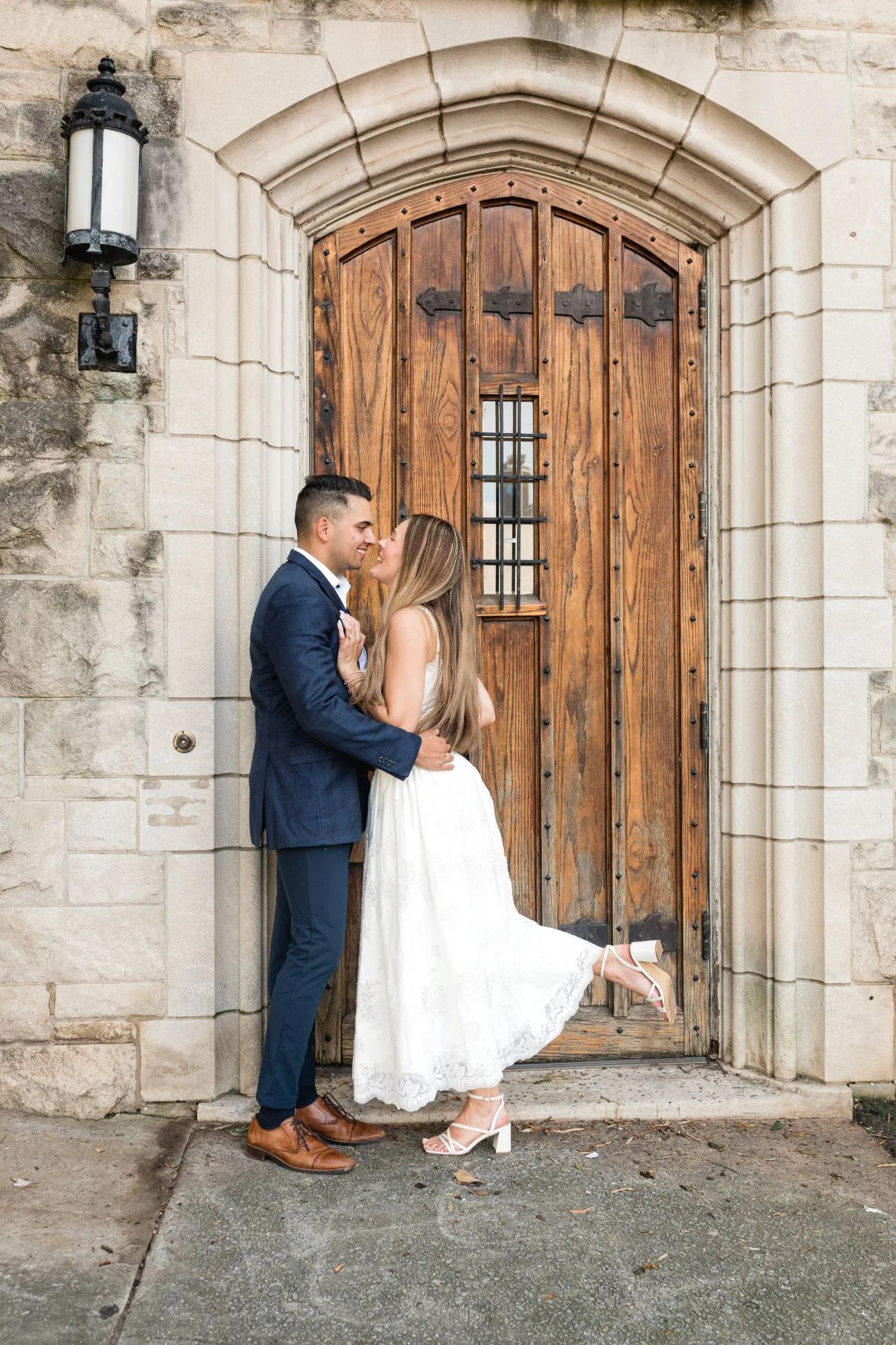 Downtown Atlanta: nose to nose at an old arched wooden door, her heel kicked up, at their engagement session near the Georgia State Capitol in Atlanta, GA